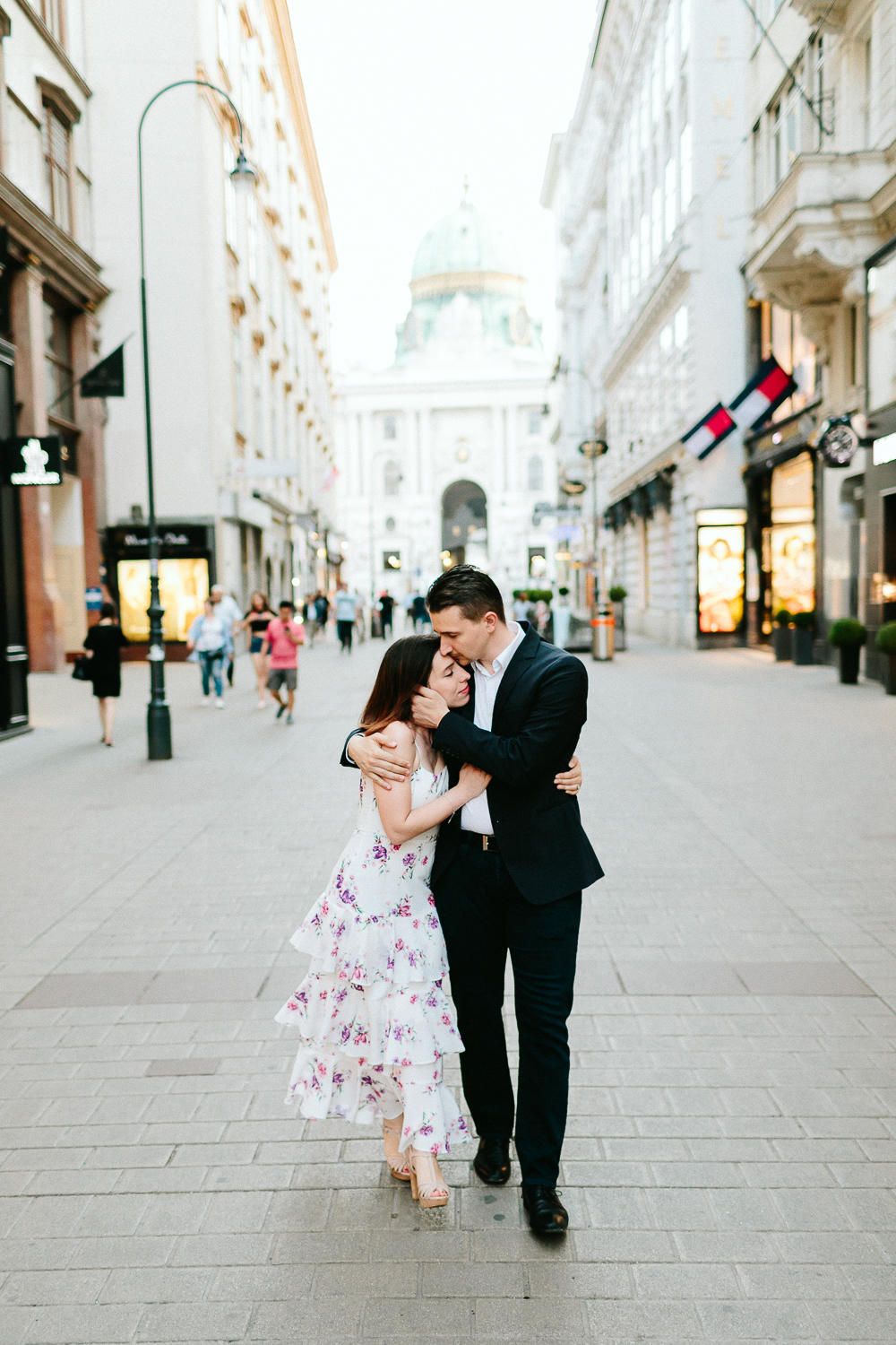 Couple sharing a romantic kiss on a European city pedestrian street with grand architecture.