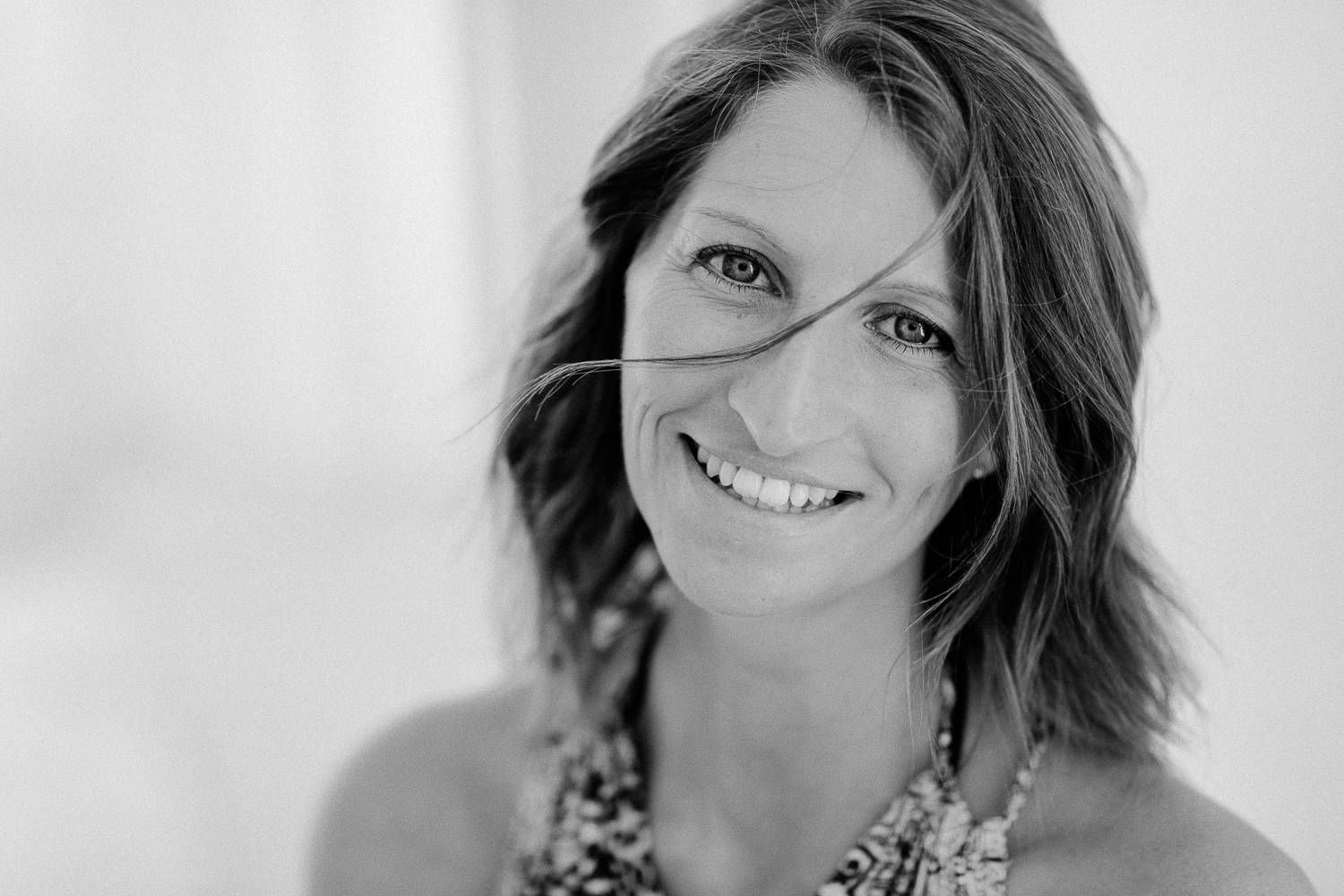 Black and white portrait of a smiling woman with short wavy hair and a floral necklace.