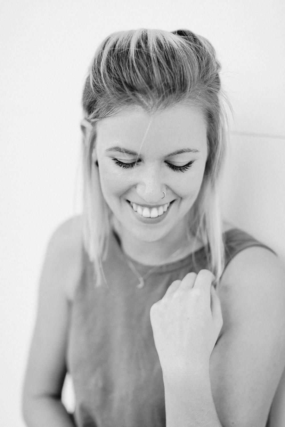 Black and white portrait of laughing blonde woman with half-up hairstyle looking downward.