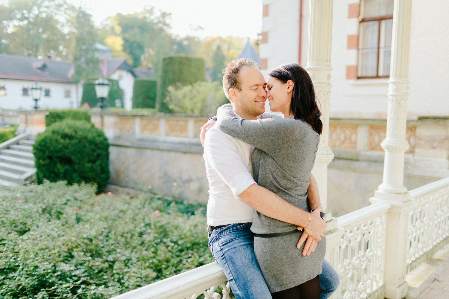 Loving couple embracing on a decorative balcony with a scenic garden backdrop.
