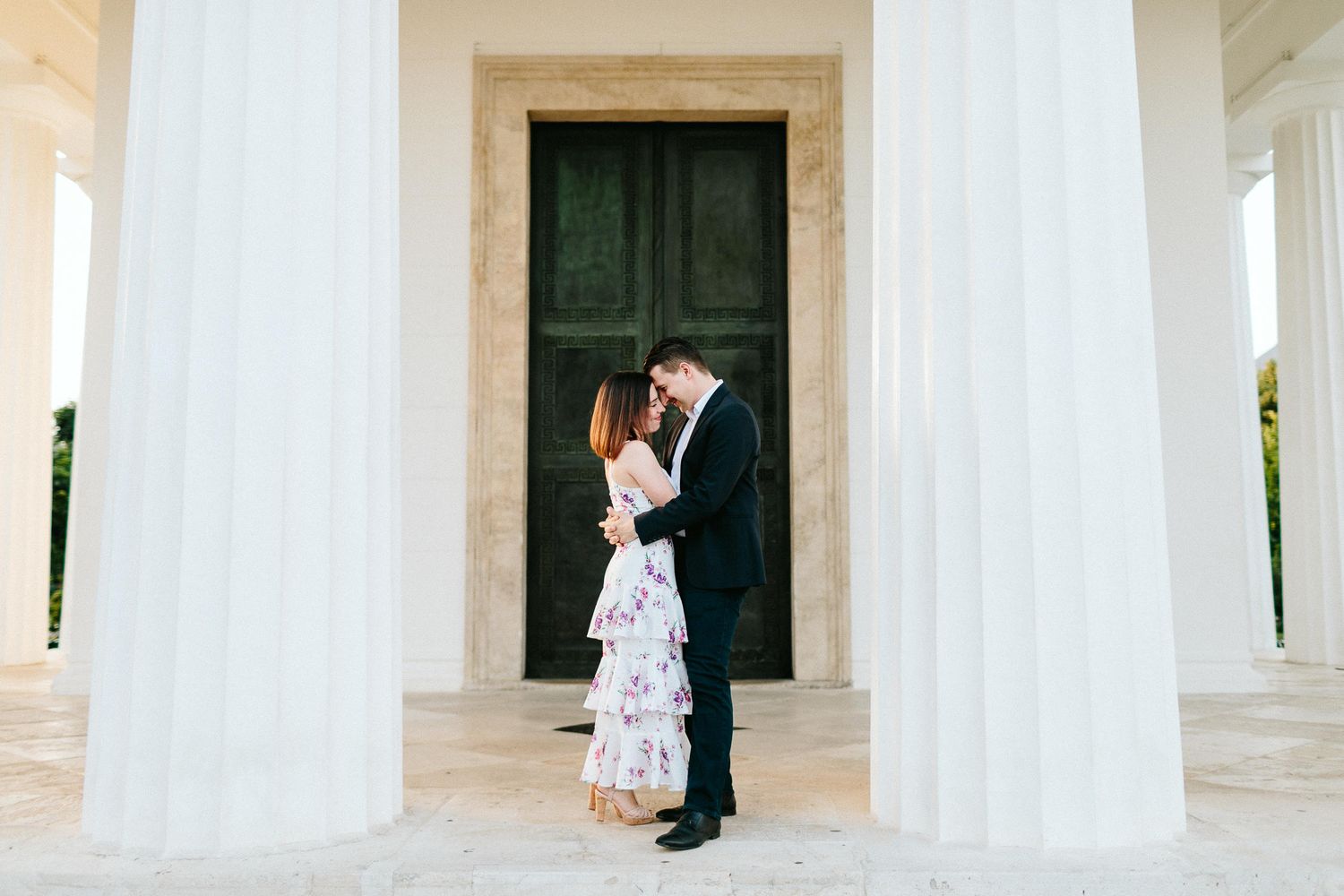 Couple sharing a romantic kiss between white columns of an elegant building.