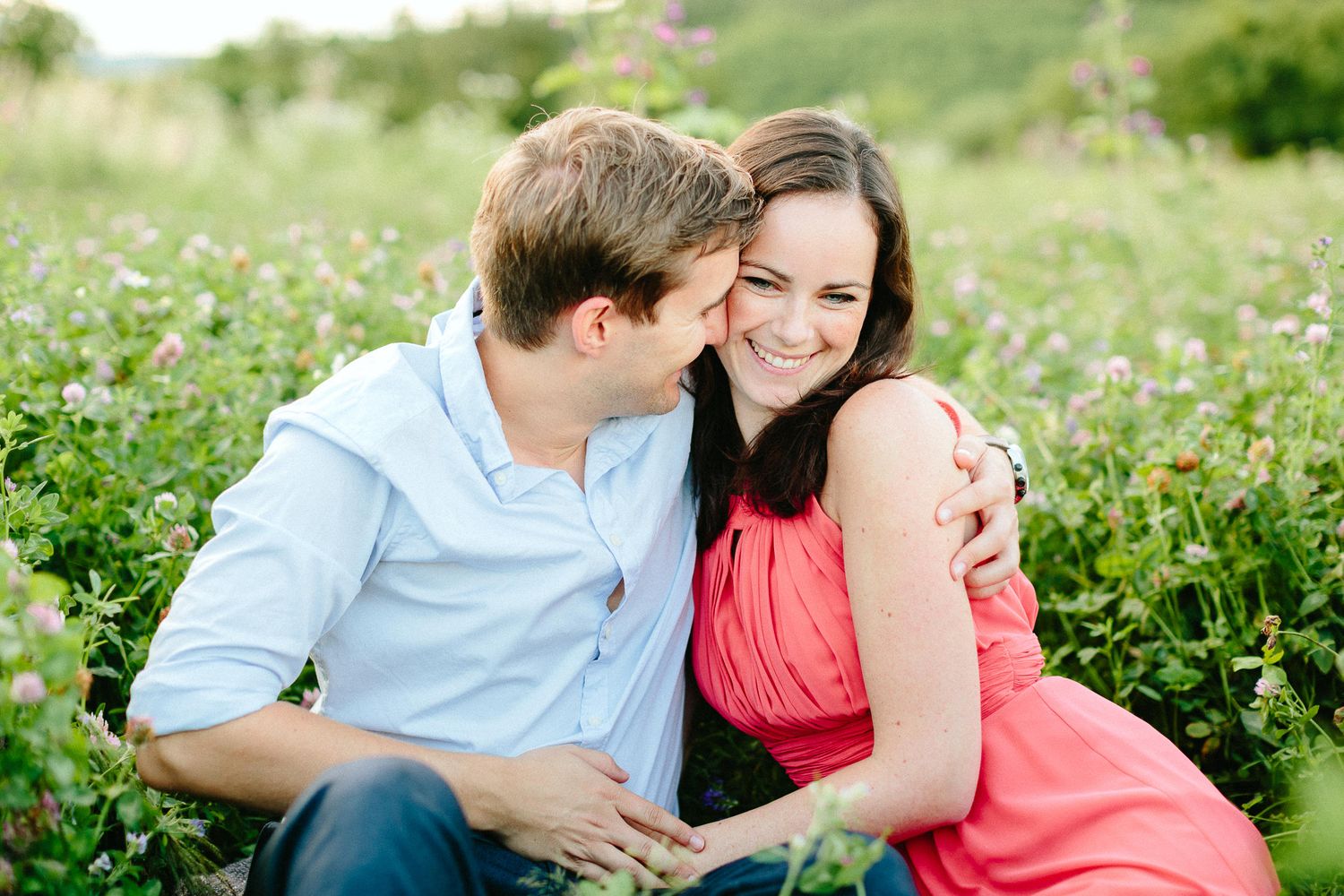 Happy couple sitting in a wildflower field, laughing and embracing warmly.