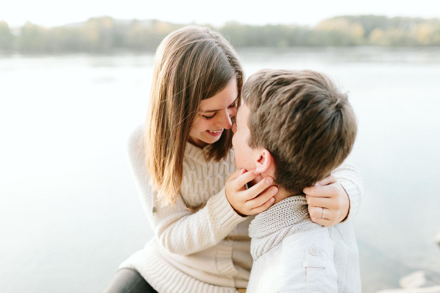 A woman tenderly embracing a man near a calm lake in soft autumn light.