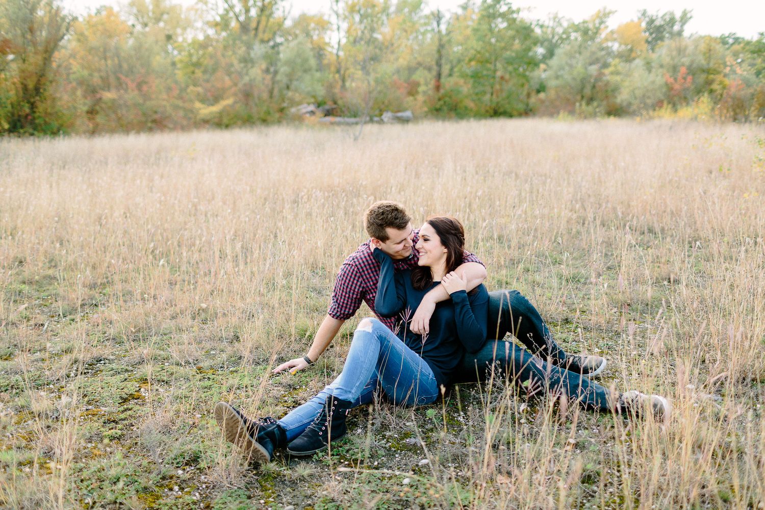 Romantic couple sitting together in a golden field of tall grass during autumn engagement session.