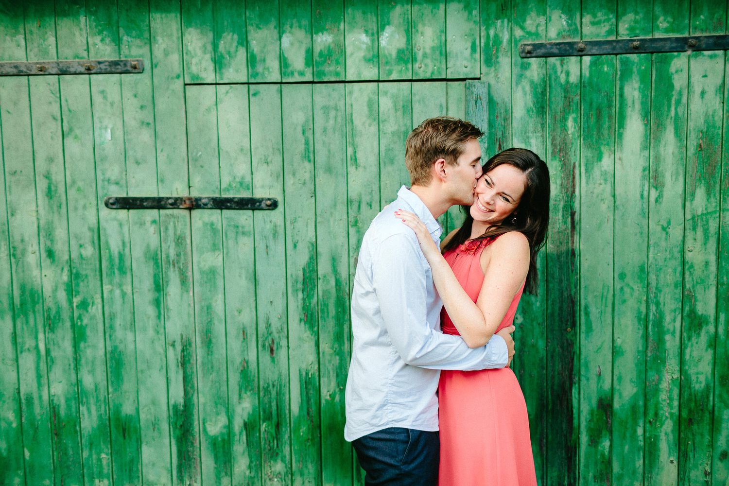 Couple sharing a tender kiss against a rustic green wooden door outdoors.