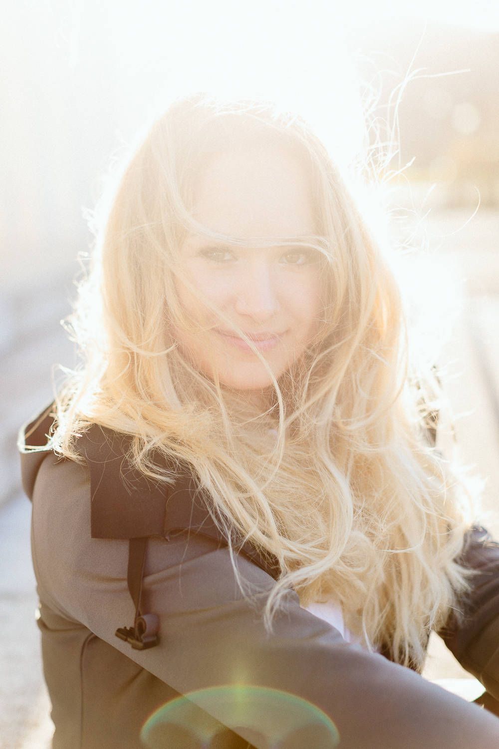 Blonde woman with windswept hair bathed in bright golden sunlight outdoors.