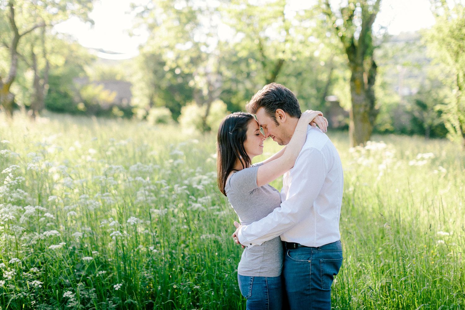 Couple embracing and nearly kissing in a lush green meadow filled with white wildflowers.