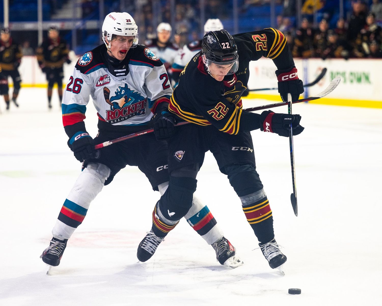 A Vancouver Giant hockey player tries to hit the puck while a Kelowna Giant player commits a hooking penalty