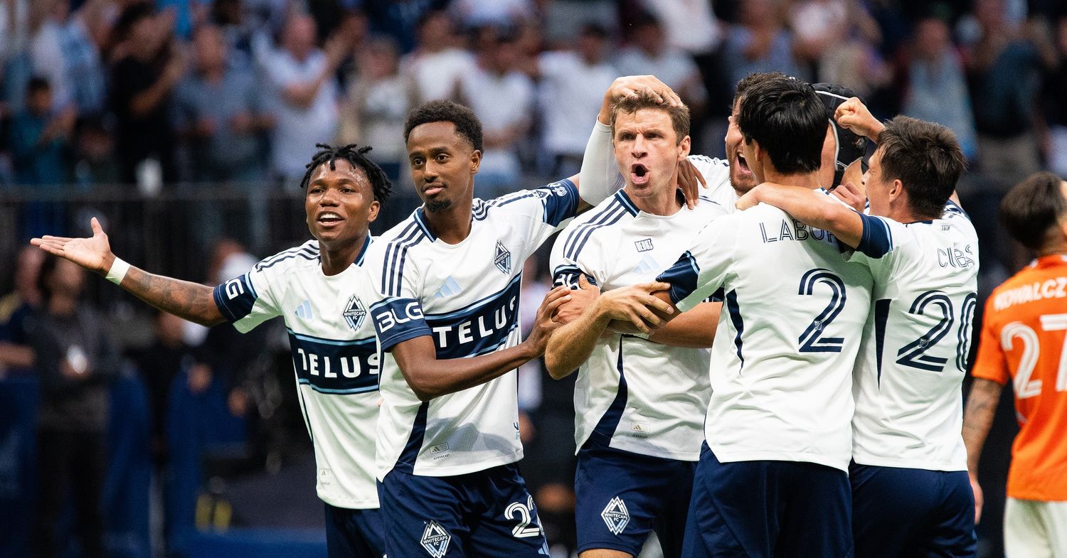 Thomas Müller of the Vancouver Whitecaps looks shocked. He is surrounded by his teammates who are hugging him and also look surprised.