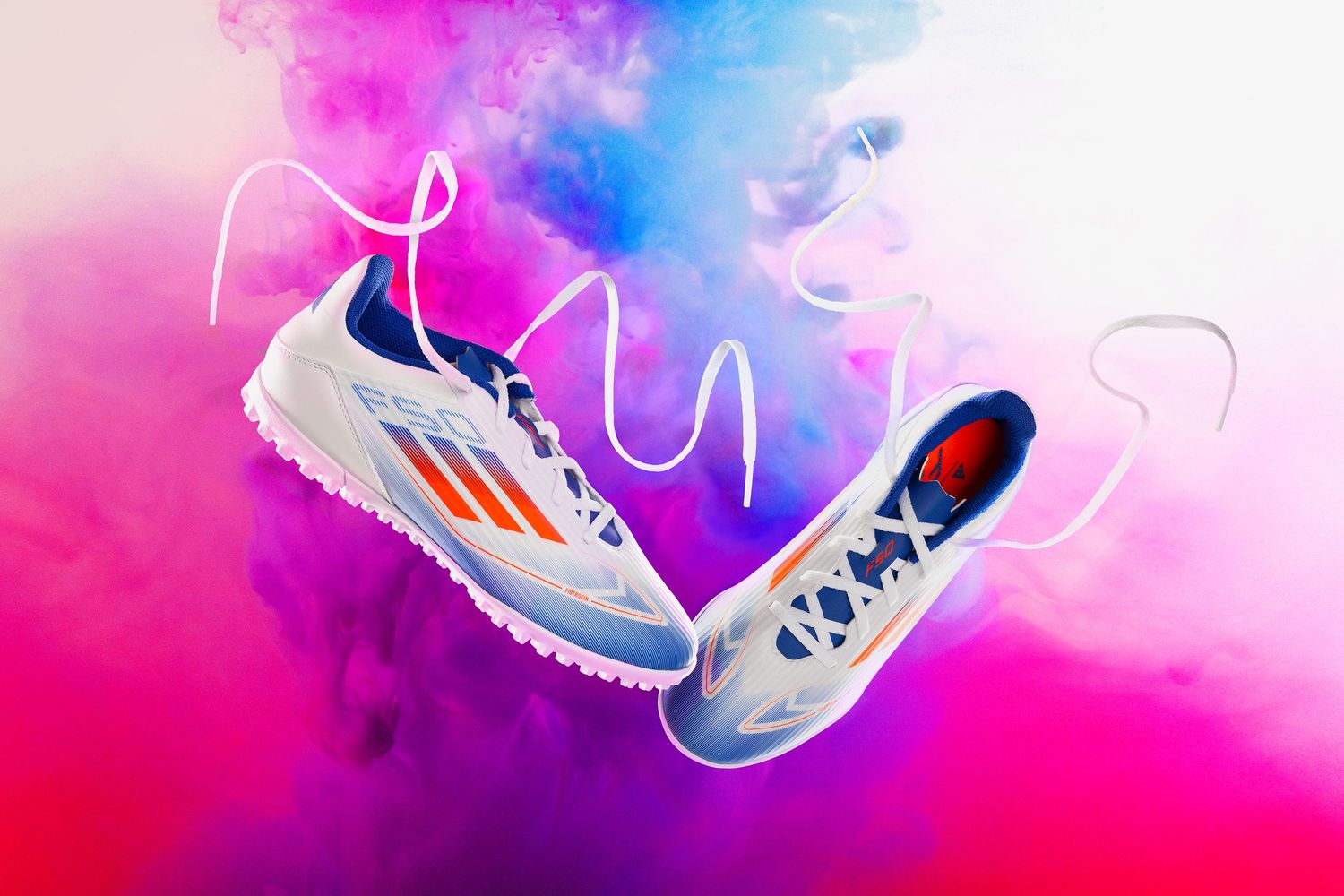 A pair of Adidas F50 soccer cleats float in the air with an explosion of colours behind them