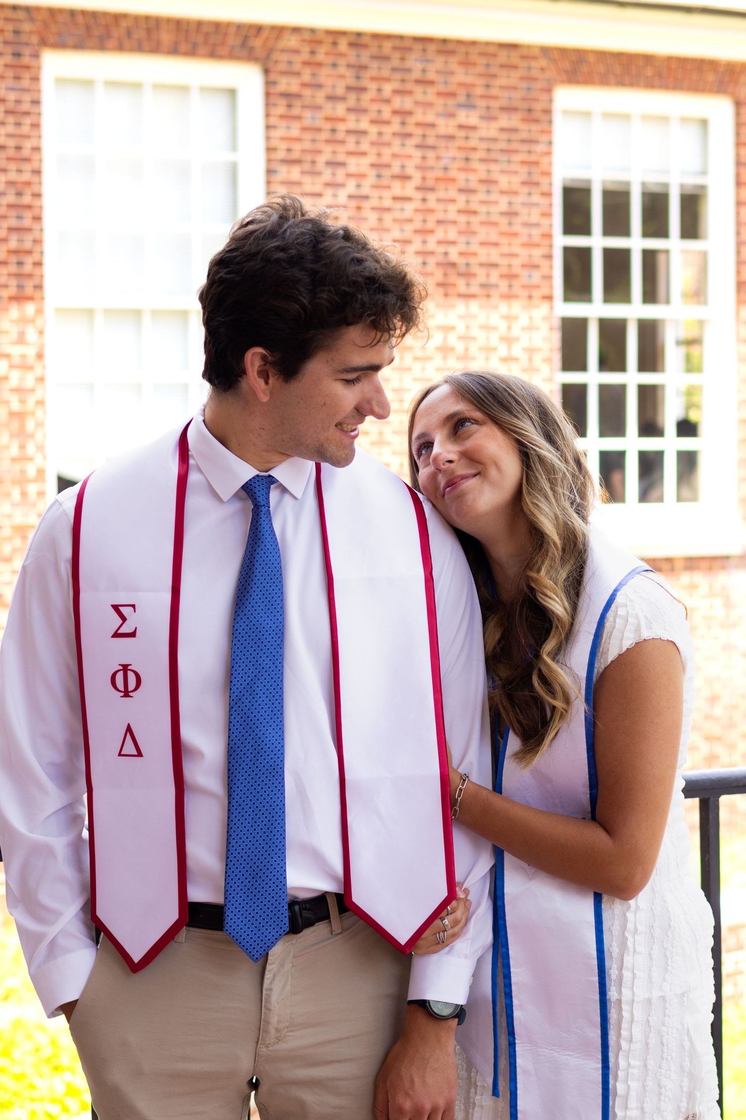 Graduates wearing Greek organization stoles embrace during photo session at the University of Delaware.