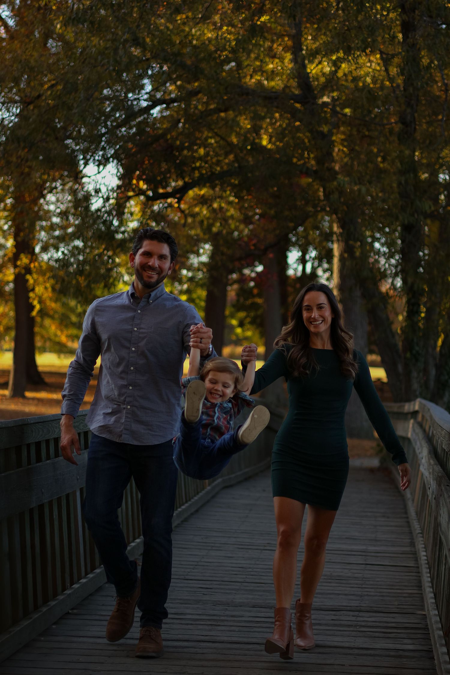 Family holds hands while walking together on wooden bridge path in park in Wilmington, Delaware