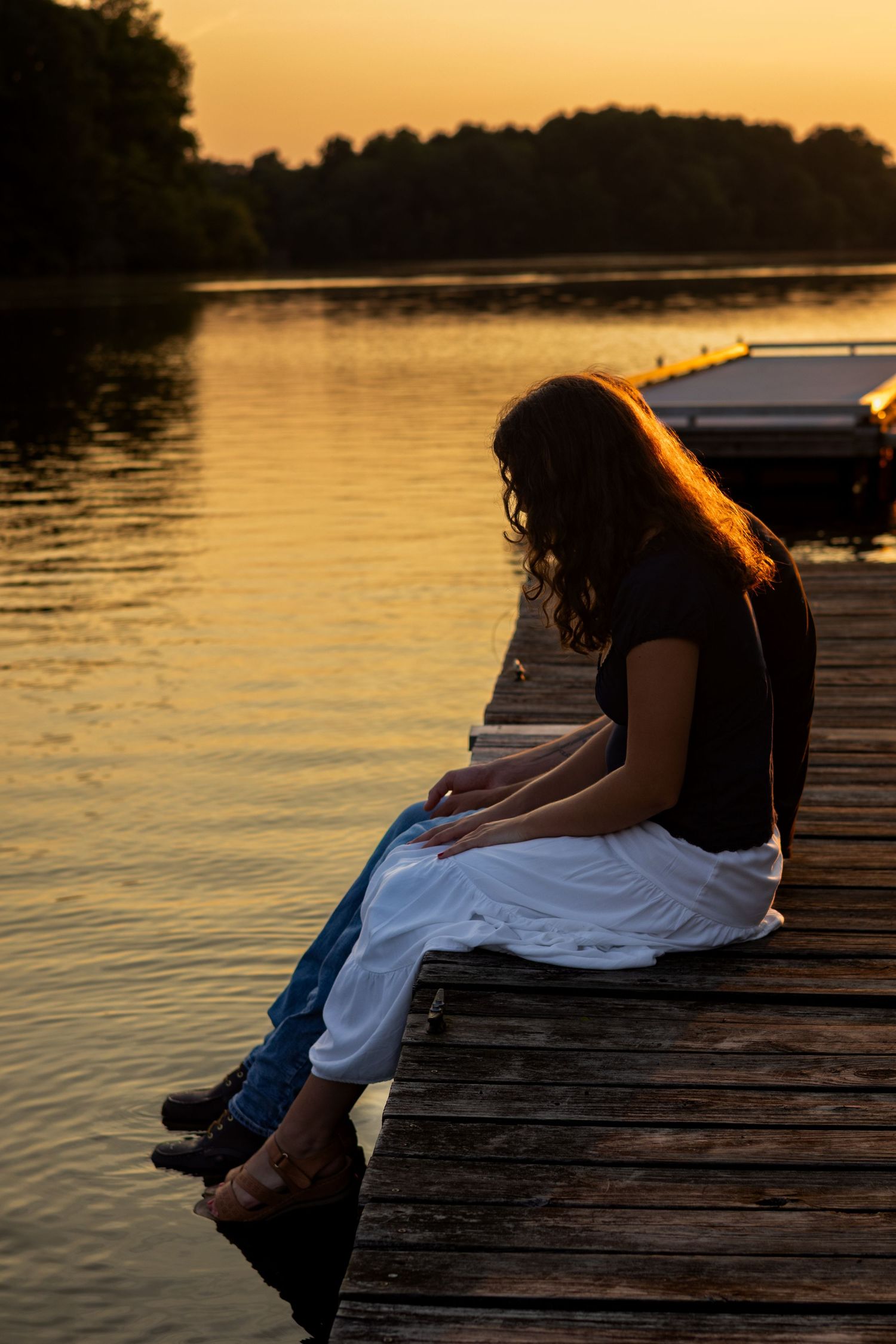 A couple sits on a wooden dock at sunset, creating a peaceful reflection on the calm lake waters in Bear, Delaware.