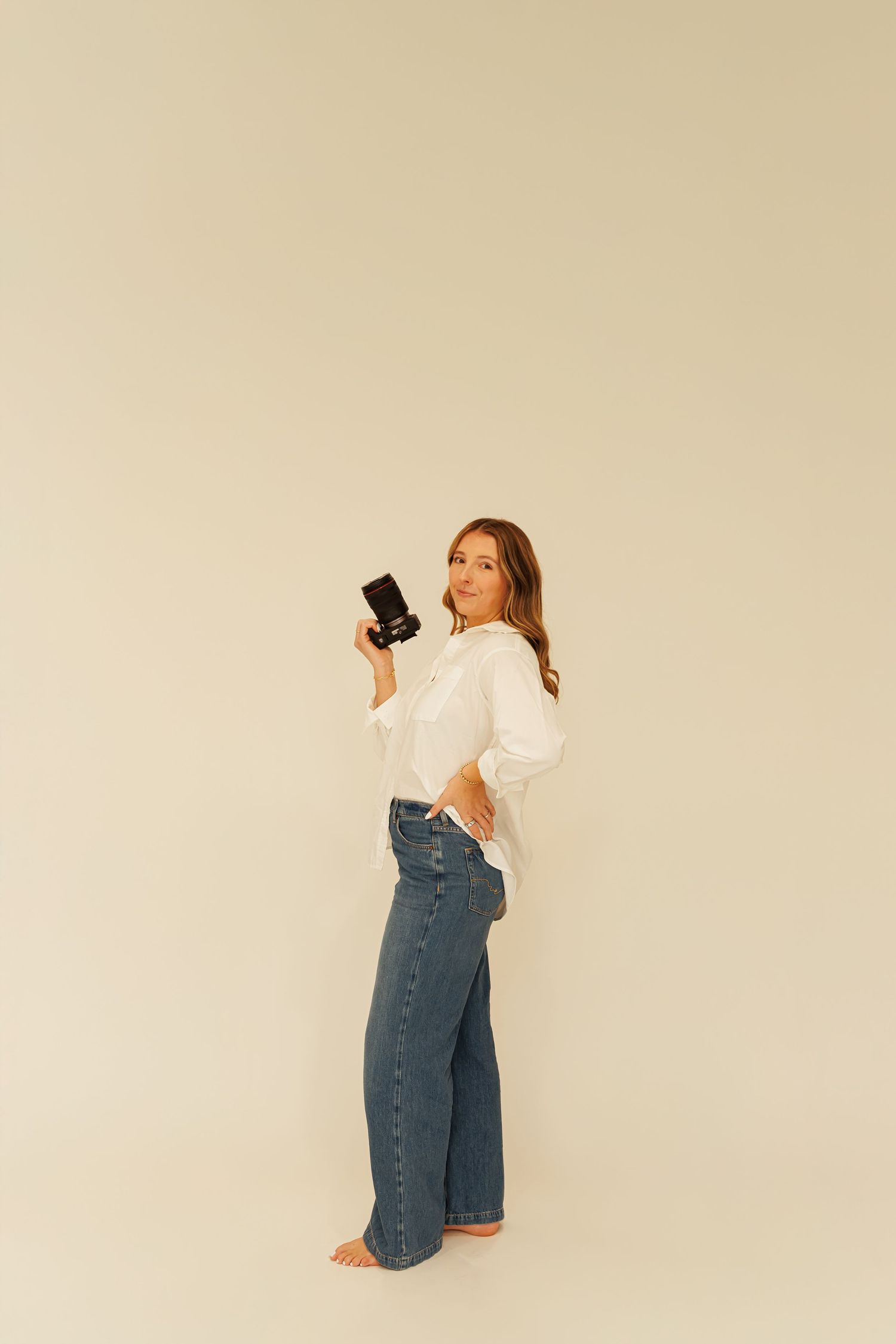 A person in denim poses playfully against a beige backdrop for Madison Adele Photography.