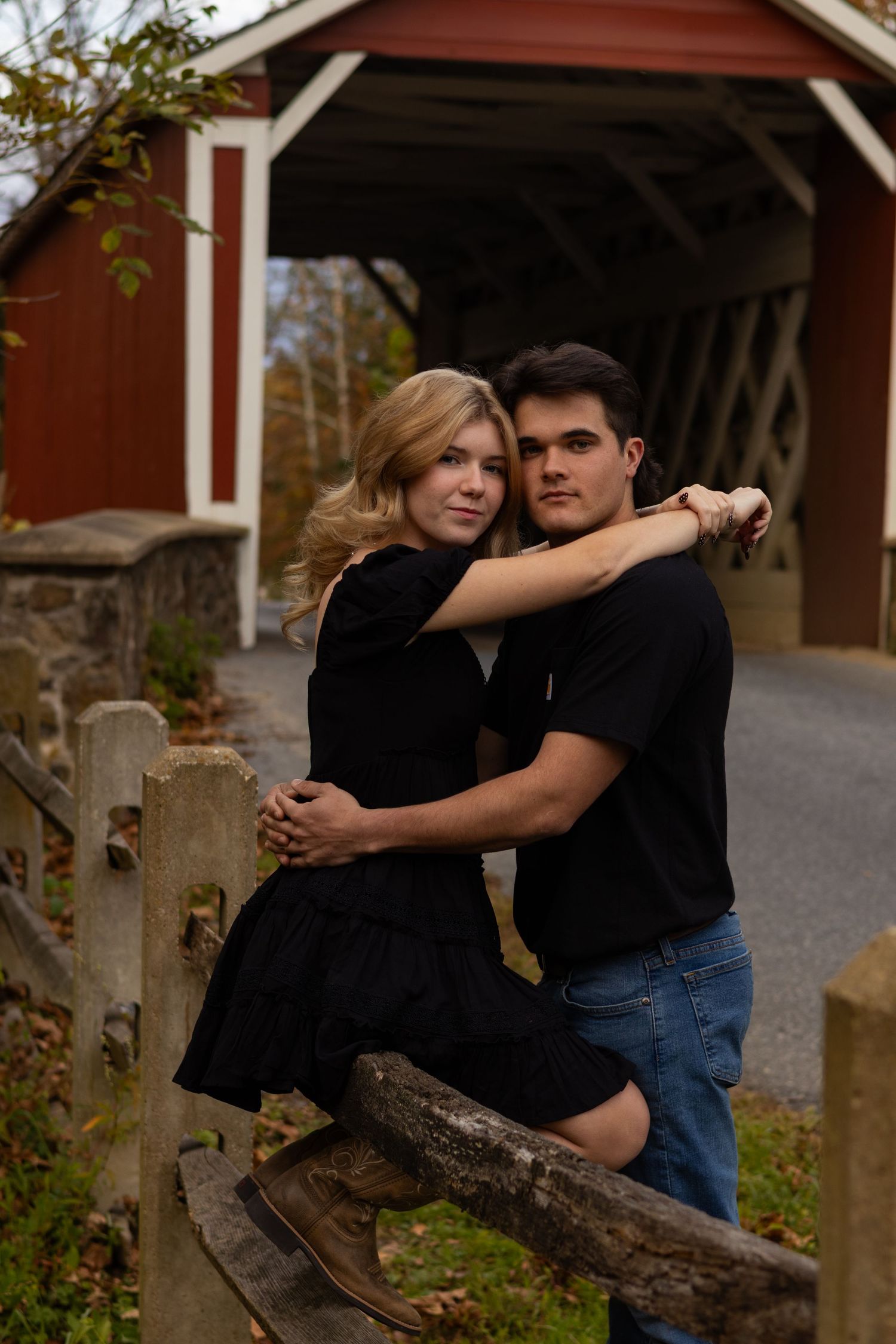 Romantic couple poses together near a rustic red covered bridge during an autumn photoshoot in Newark, Delaware.