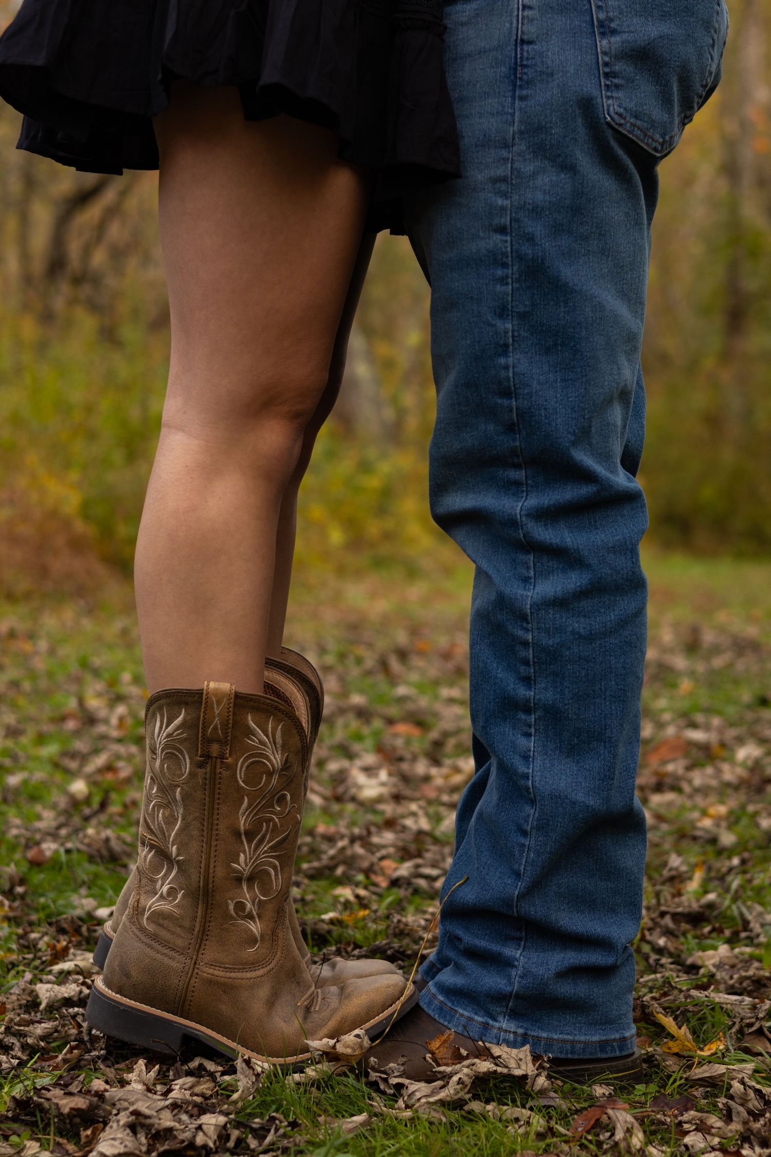 Close-up of cowboy boots and jeans showing couple's feet on autumn leaves in Newark, Delaware.