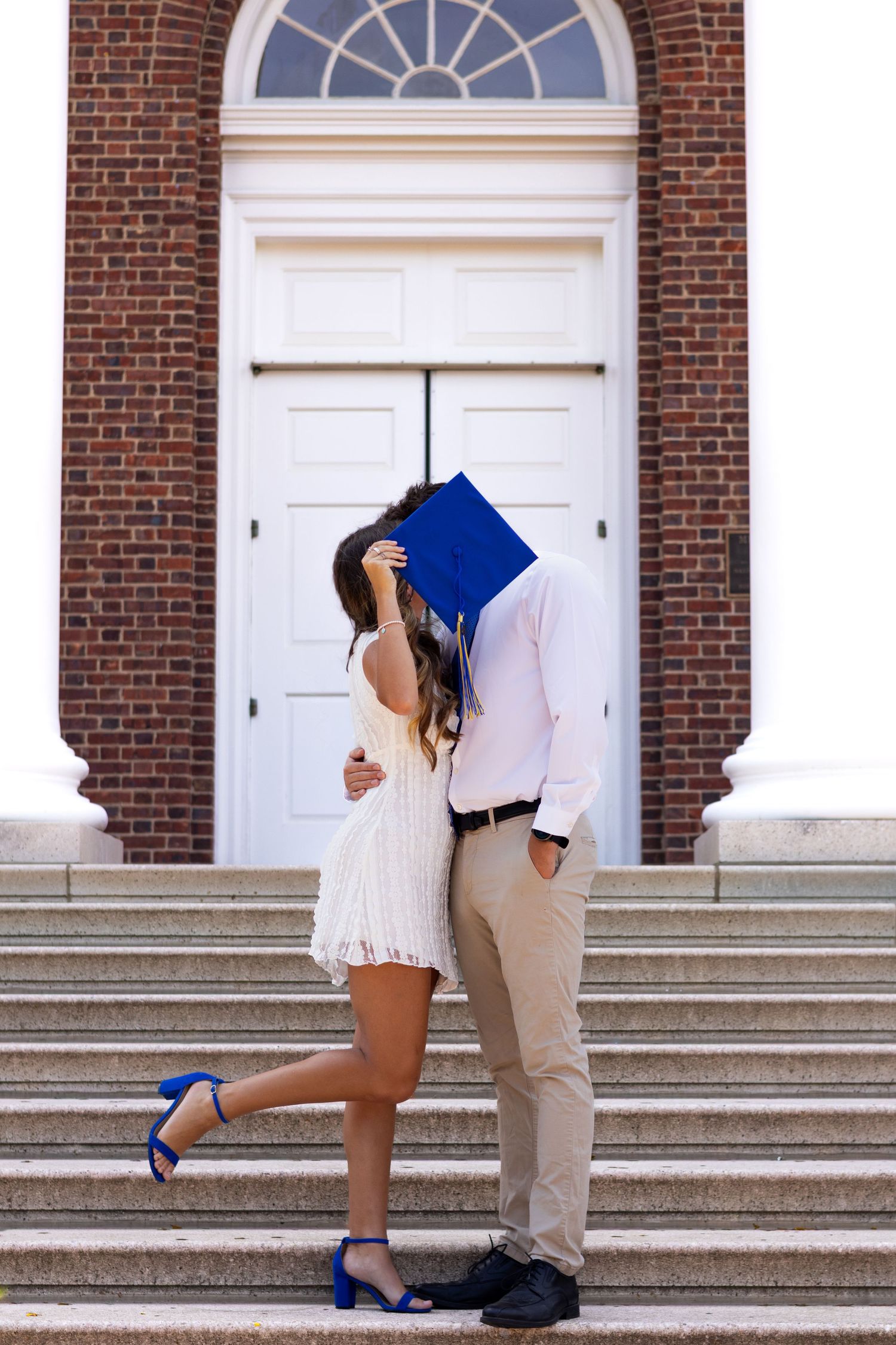 Romantic graduation photo sequence on brick building steps with blue cap at the University of Delaware.