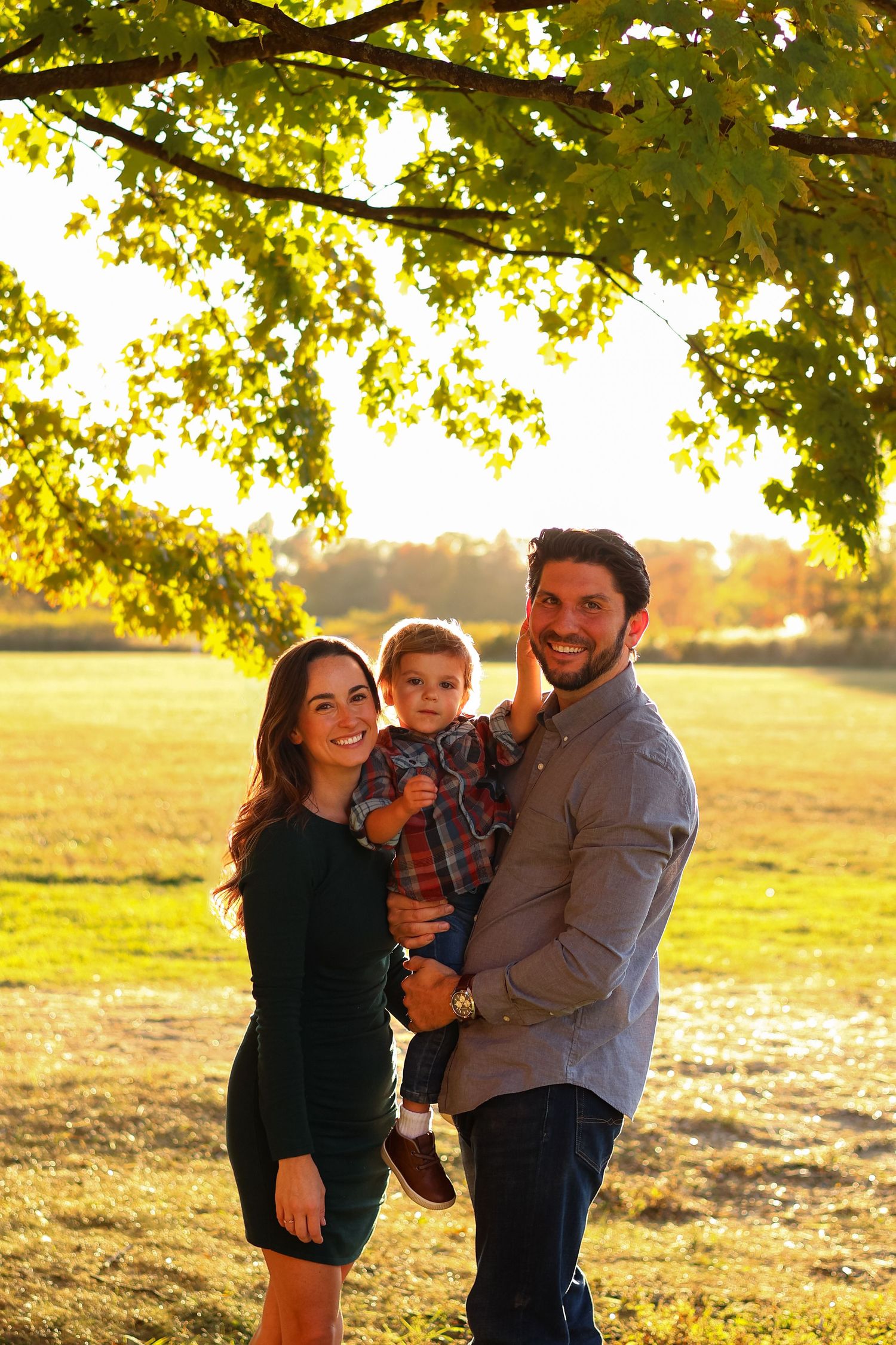 Family of three poses together in a sunlit field during golden hour in Wilmington, Delaware.