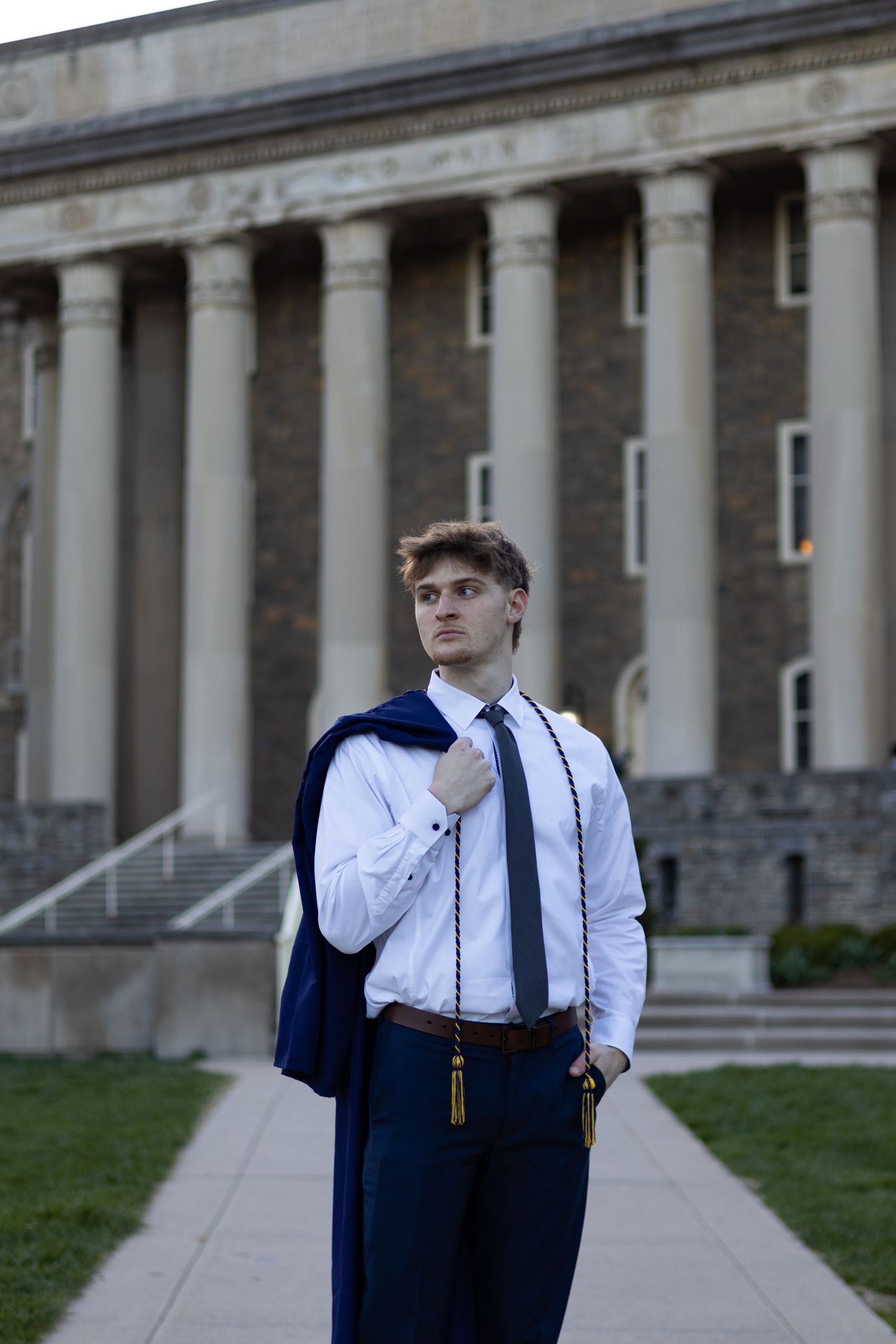 Graduate in navy academic regalia stands before row of classical columns at Penn State University.