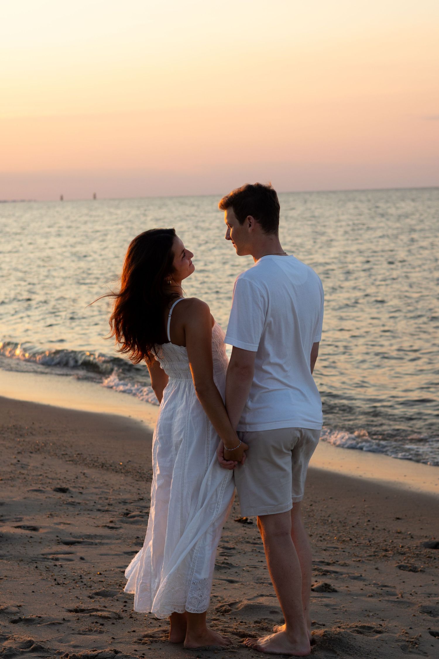 A romantic beach engagement photoshoot silhouetted against the setting sun and ocean waves in Lewes Beach, Delaware.