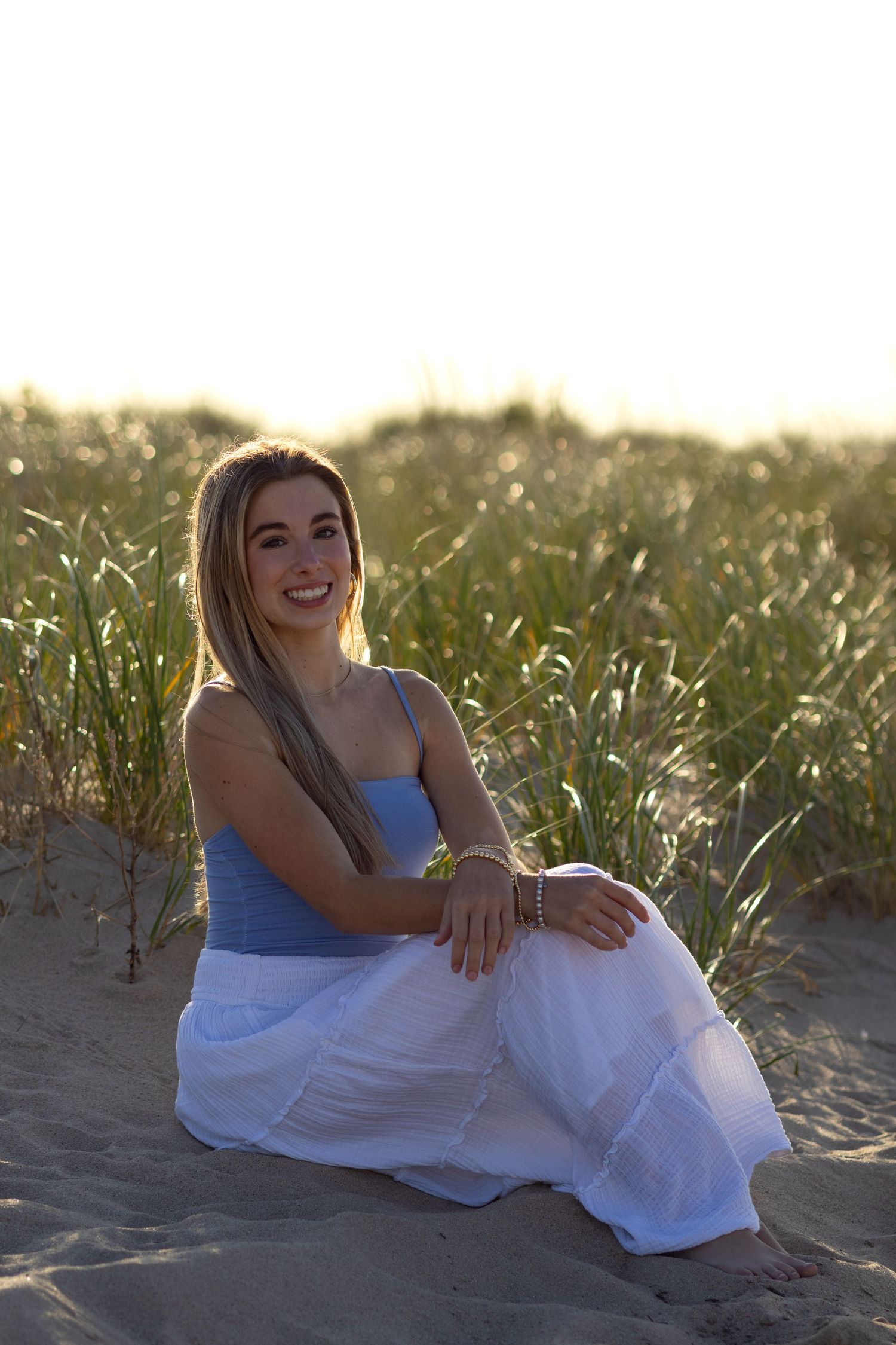 Person in white dress poses on sandy beach during sunset for senior photos in Lewes, Delaware.