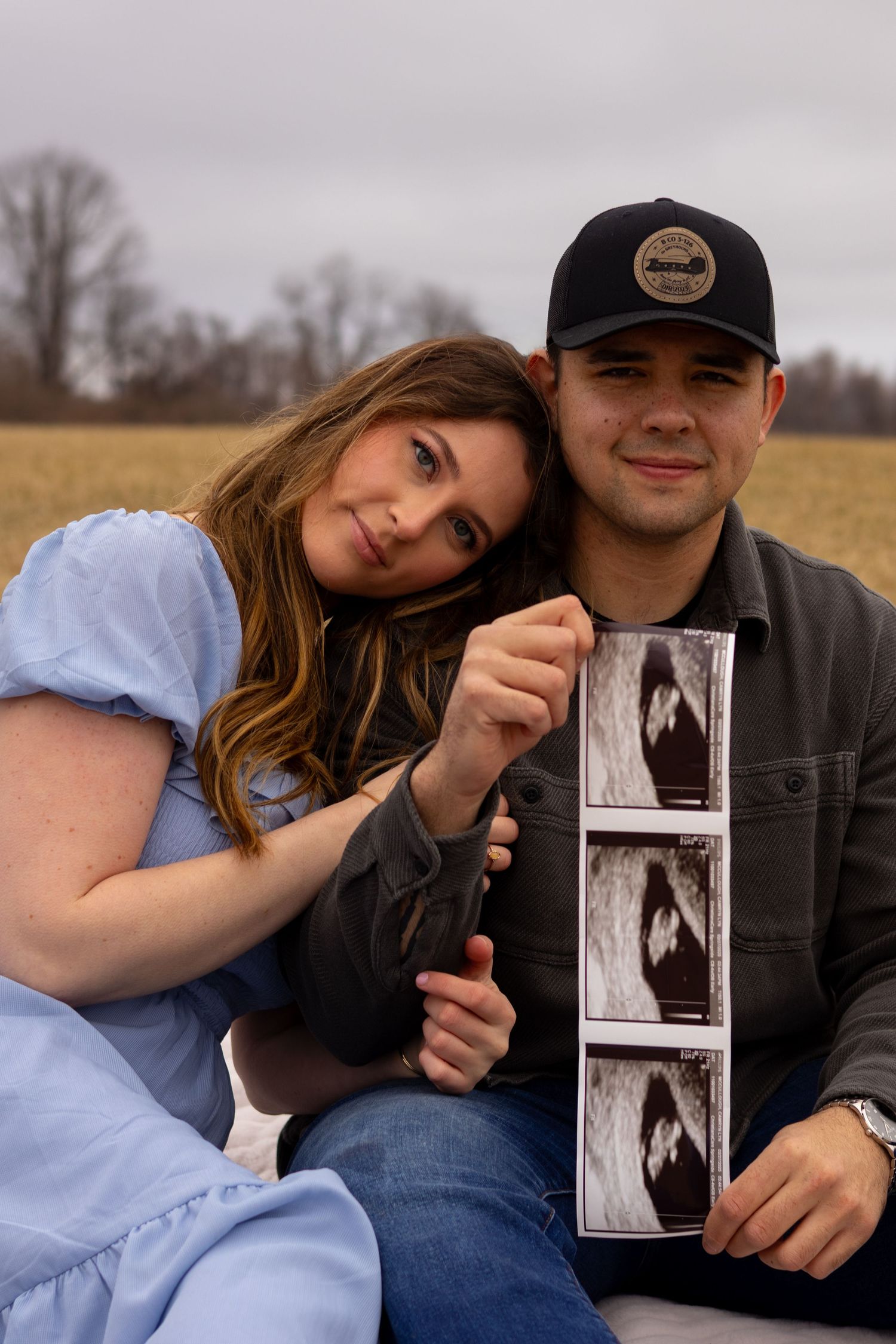 A couple poses with ultrasound photos in a field during autumn in Elkton, Maryland.