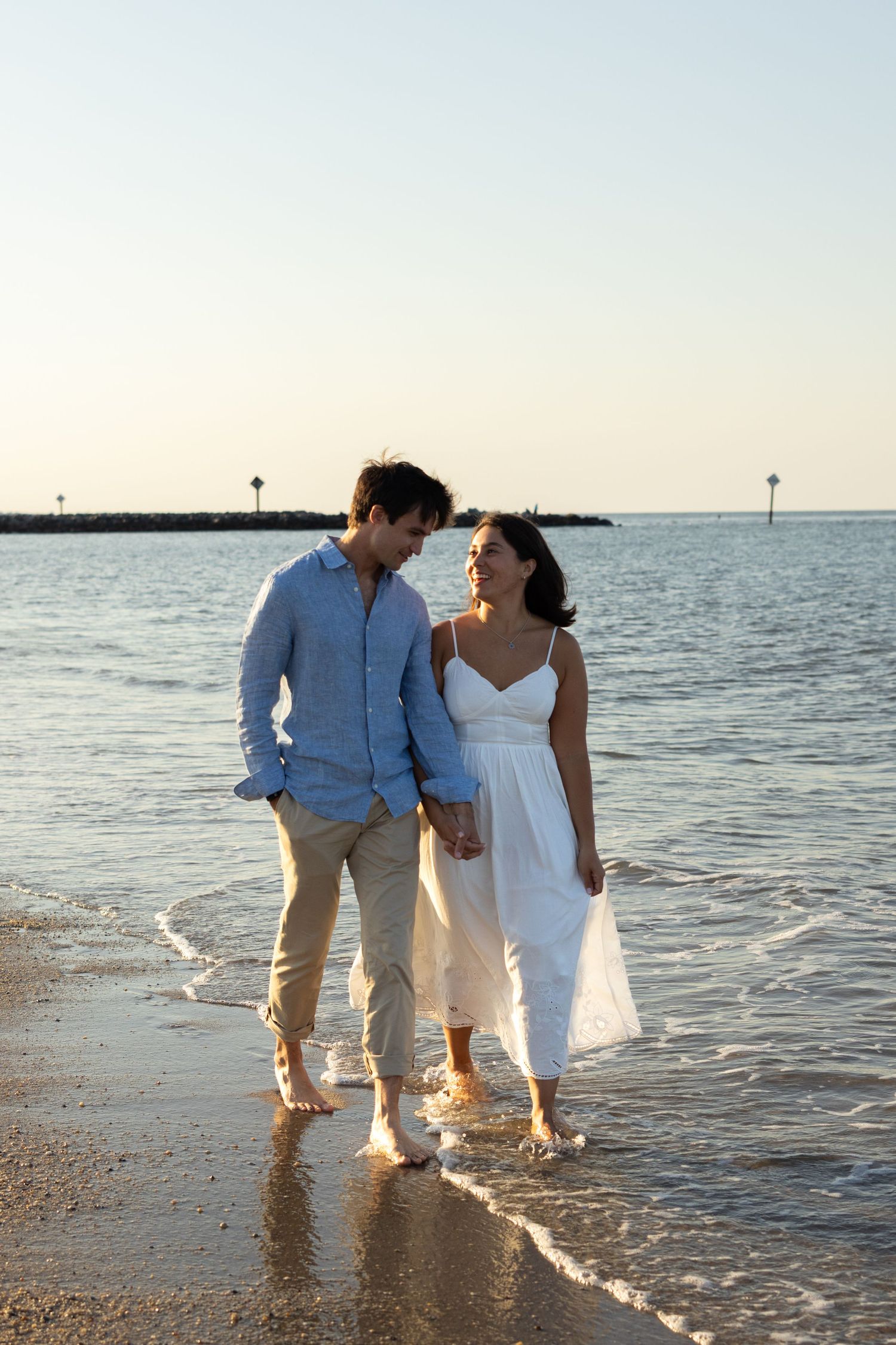 Couple walking along the shoreline at sunset in coordinated beach attire in Lewes, Delaware.