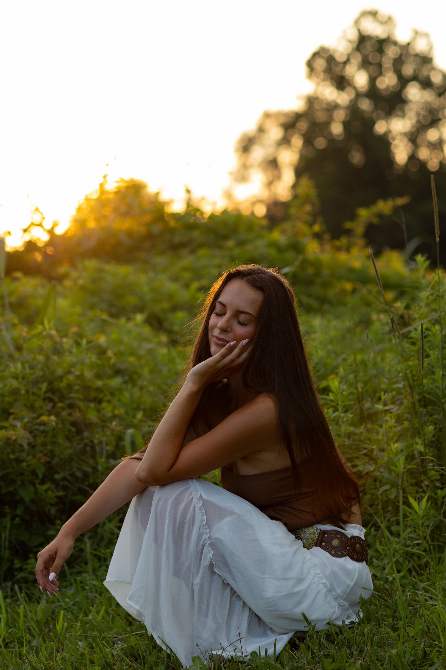 Woman in white dress resting in field during golden hour sunset in Wilmington, Delaware.