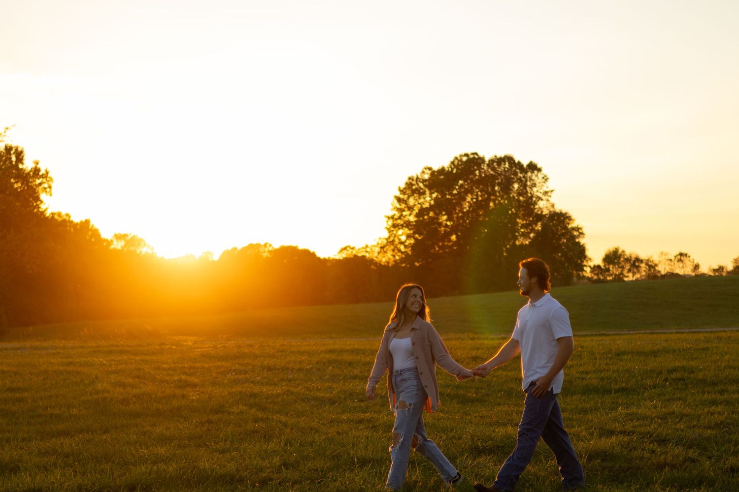 Couple walking hand in hand through field at sunset in Elkton, Maryland.