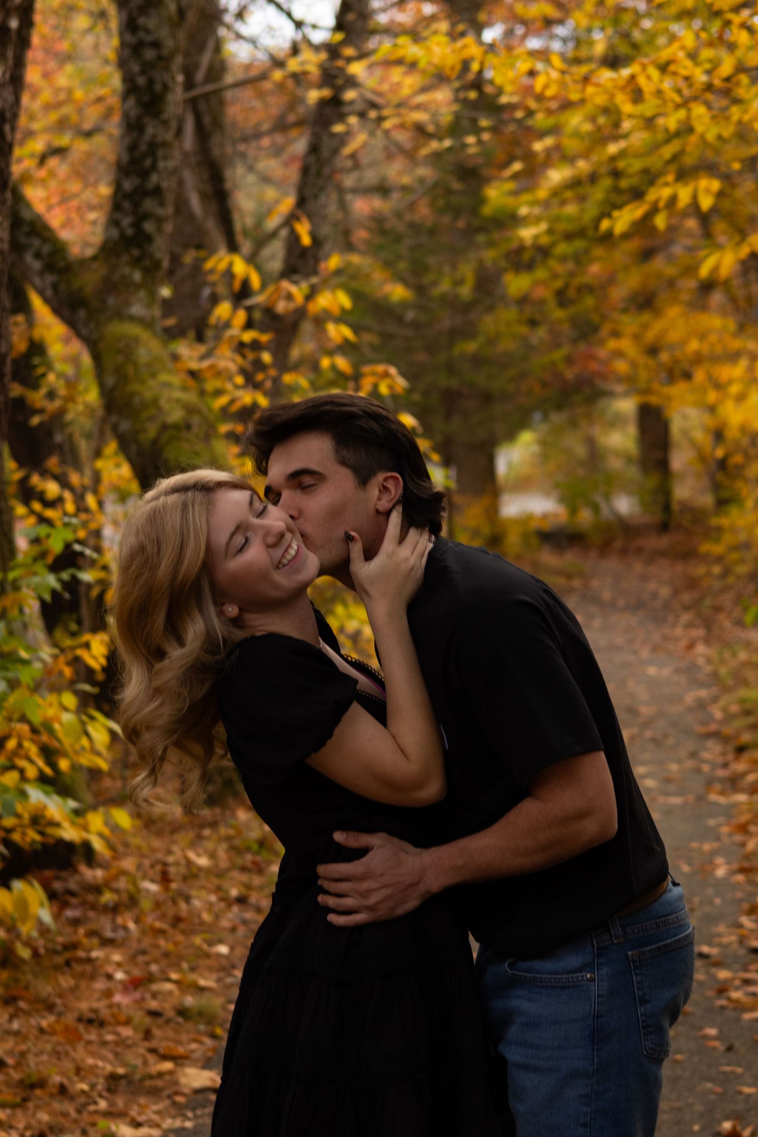 Intimate moment shared between couple on leaf-covered path in autumn woods in Newark, Delaware.