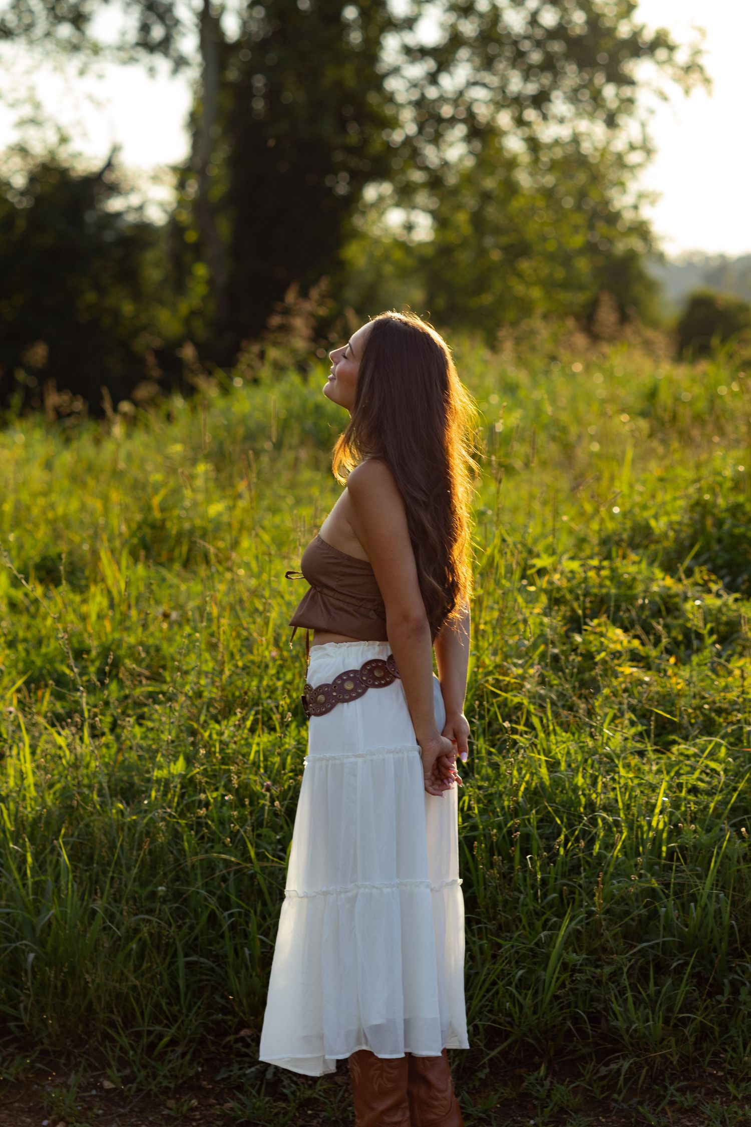 Person in white dress stands in sunlit field during golden hour portrait session in Wilmington, Delaware.