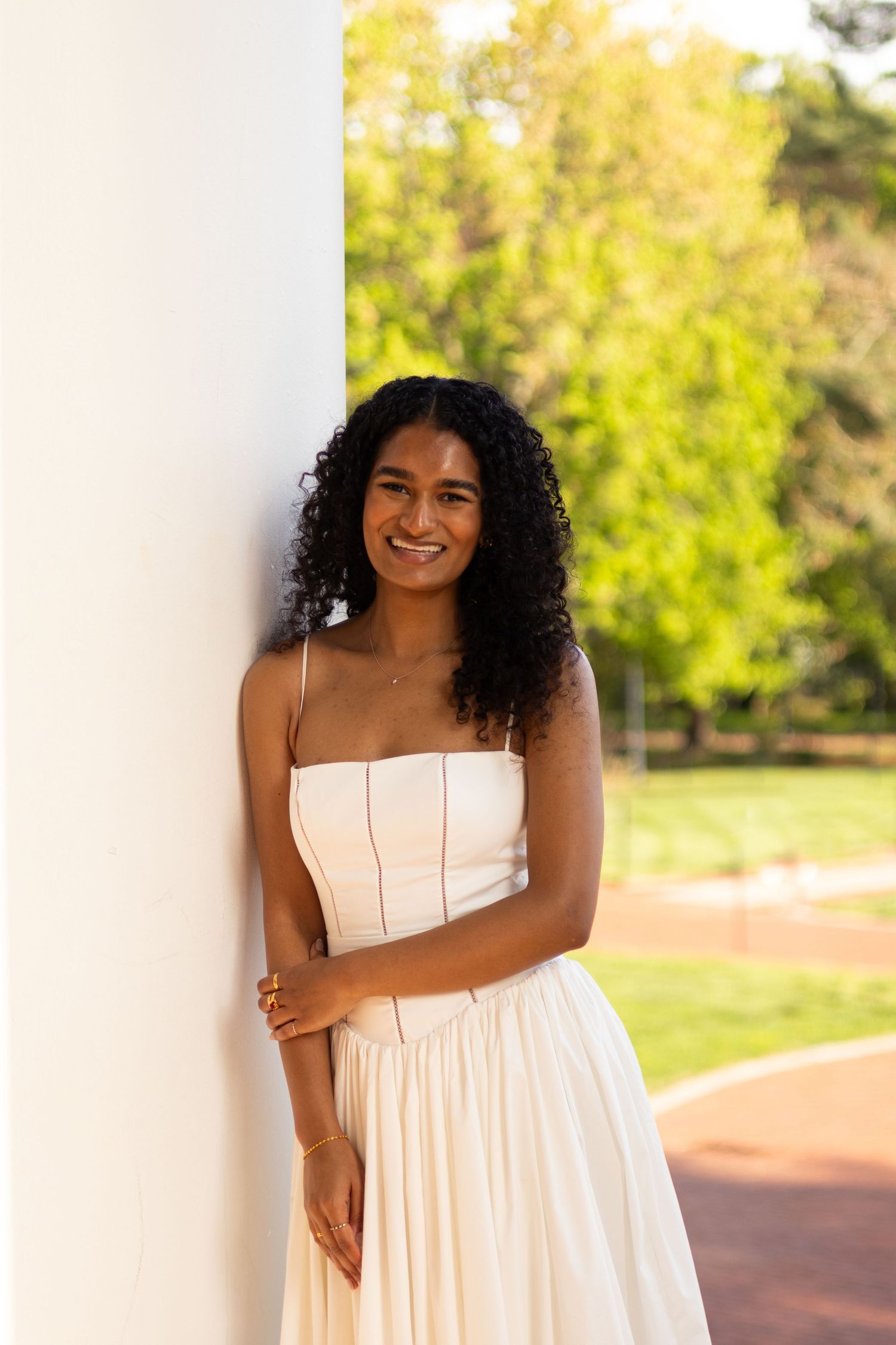 A series of joyful portraits in a white sundress against a sunny outdoor background at the University of Delaware.