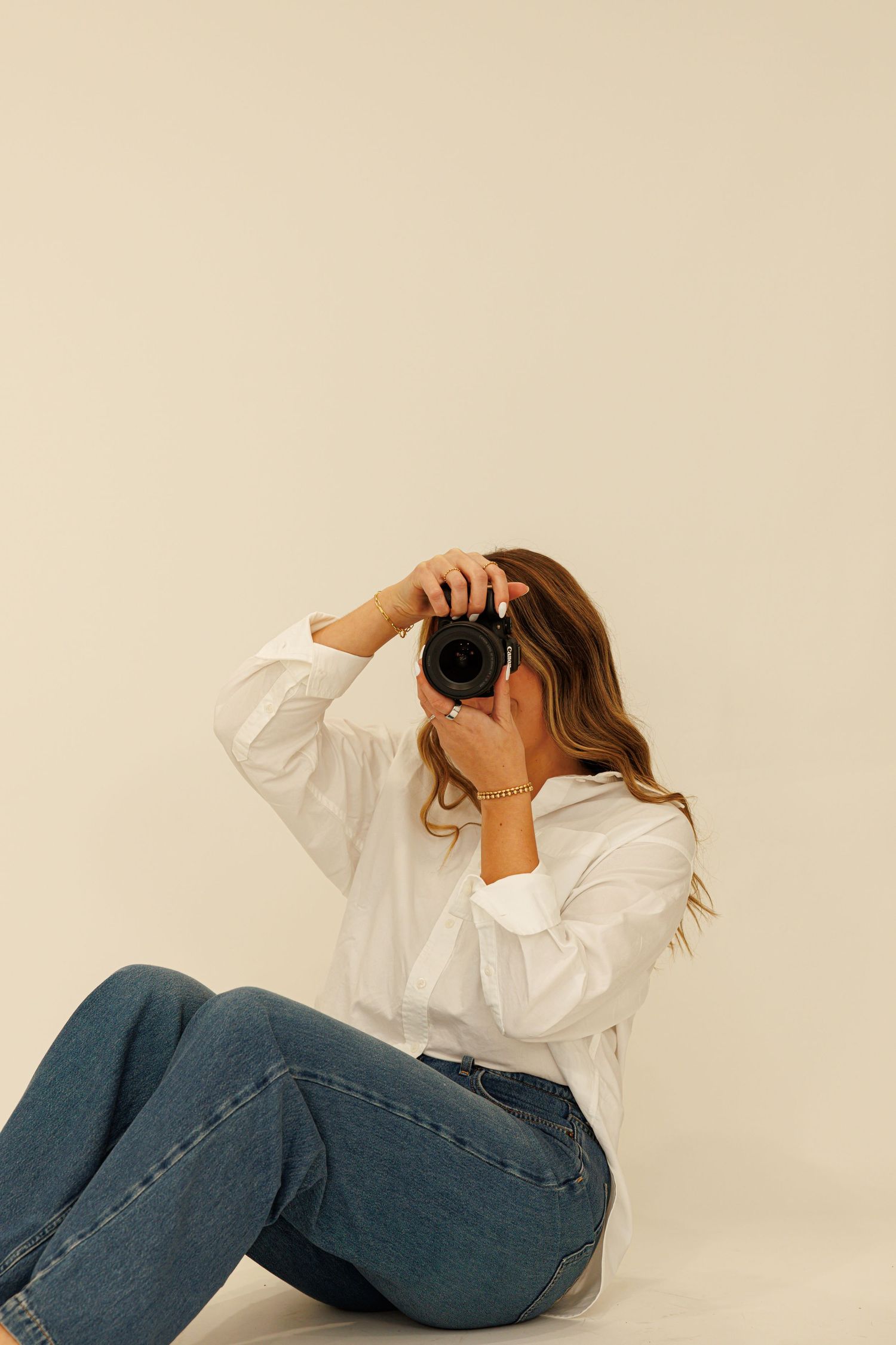 Person in white blouse and jeans poses playfully on beige background.