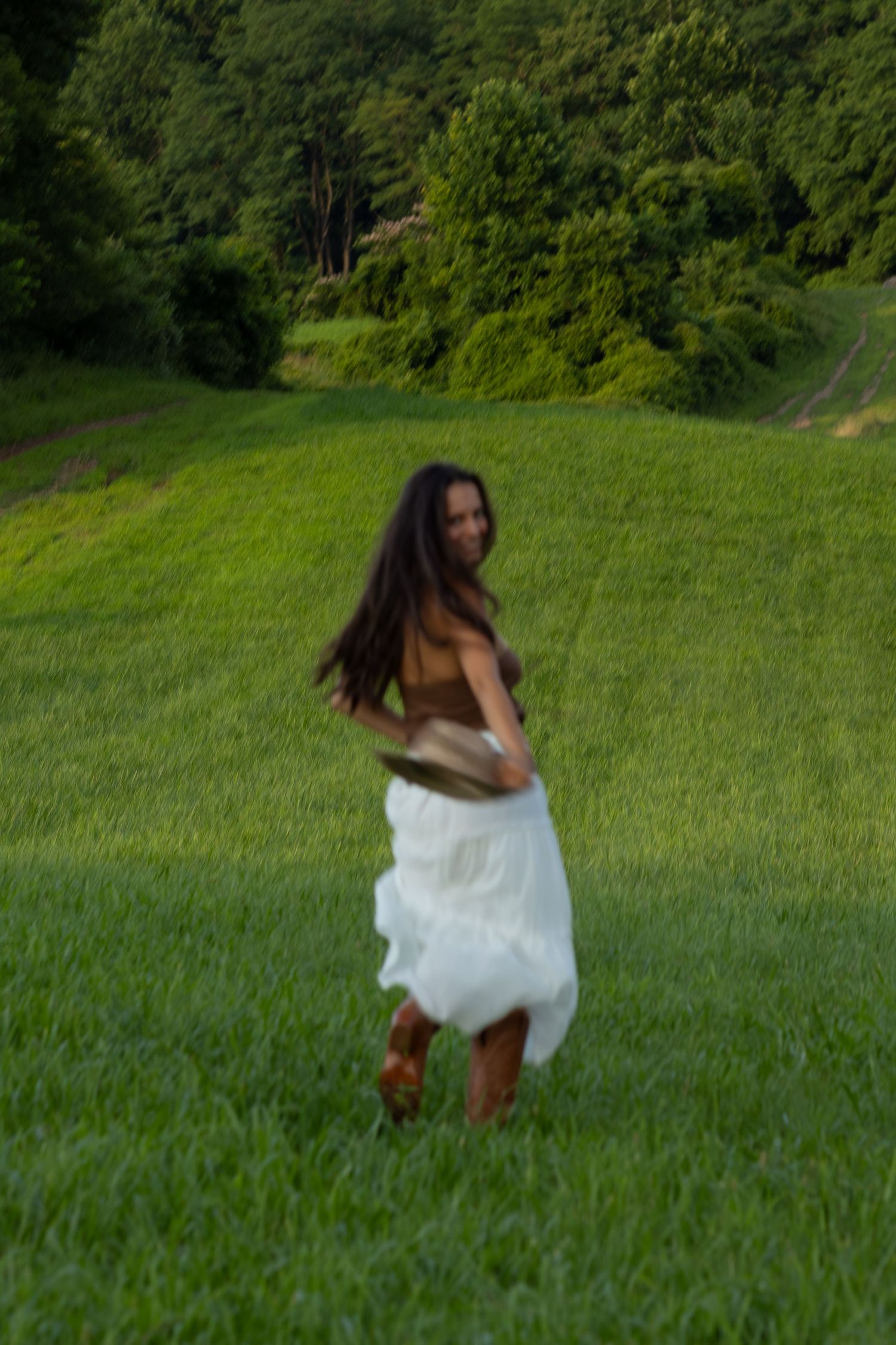 Twirling motion shot in white dress and boots against green hillside background in Wilmington, Delaware.