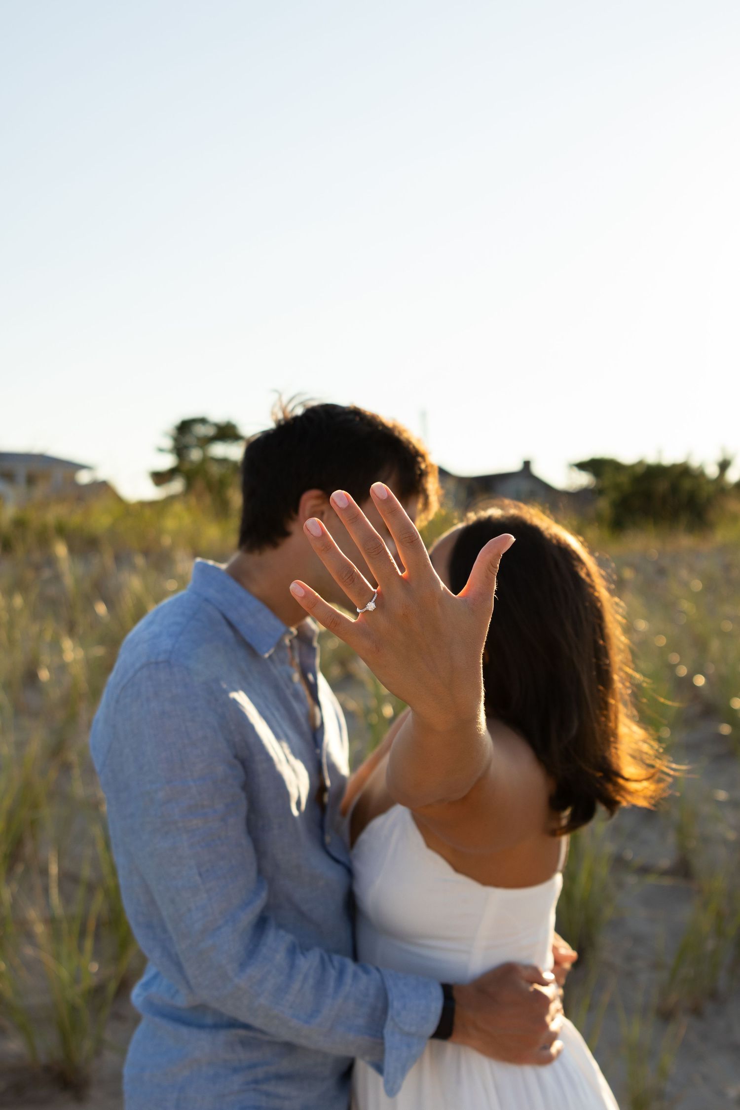 A couple sharing a romantic sunset moment on the beach while showing off an engagement ring in Lewes, Delaware.
