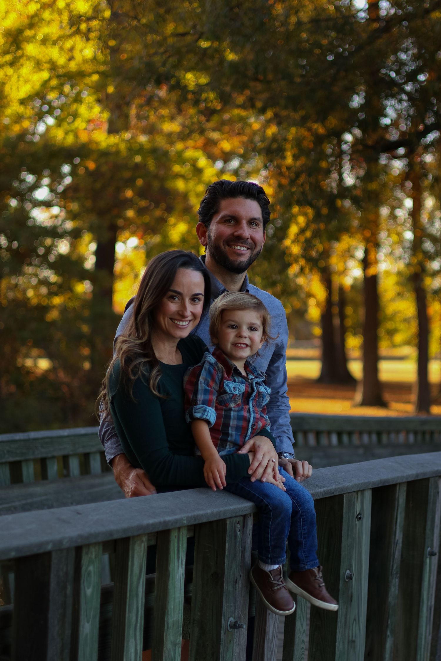 Family sits together on wooden bridge railing during golden hour in park in Wilmington, Delaware