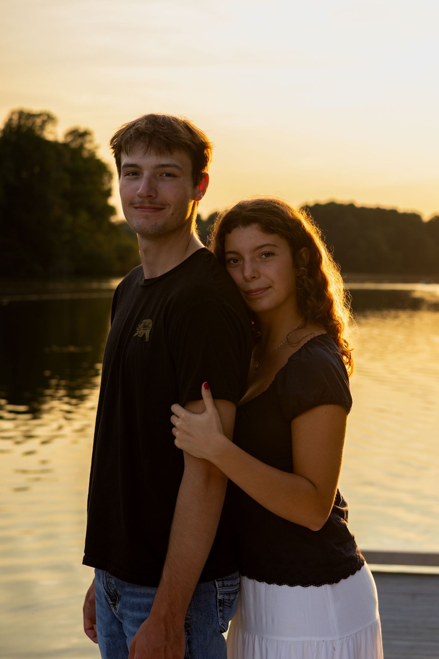 A couple embraces by the waterfront during a golden sunset with trees in the background in Bear, Delaware.