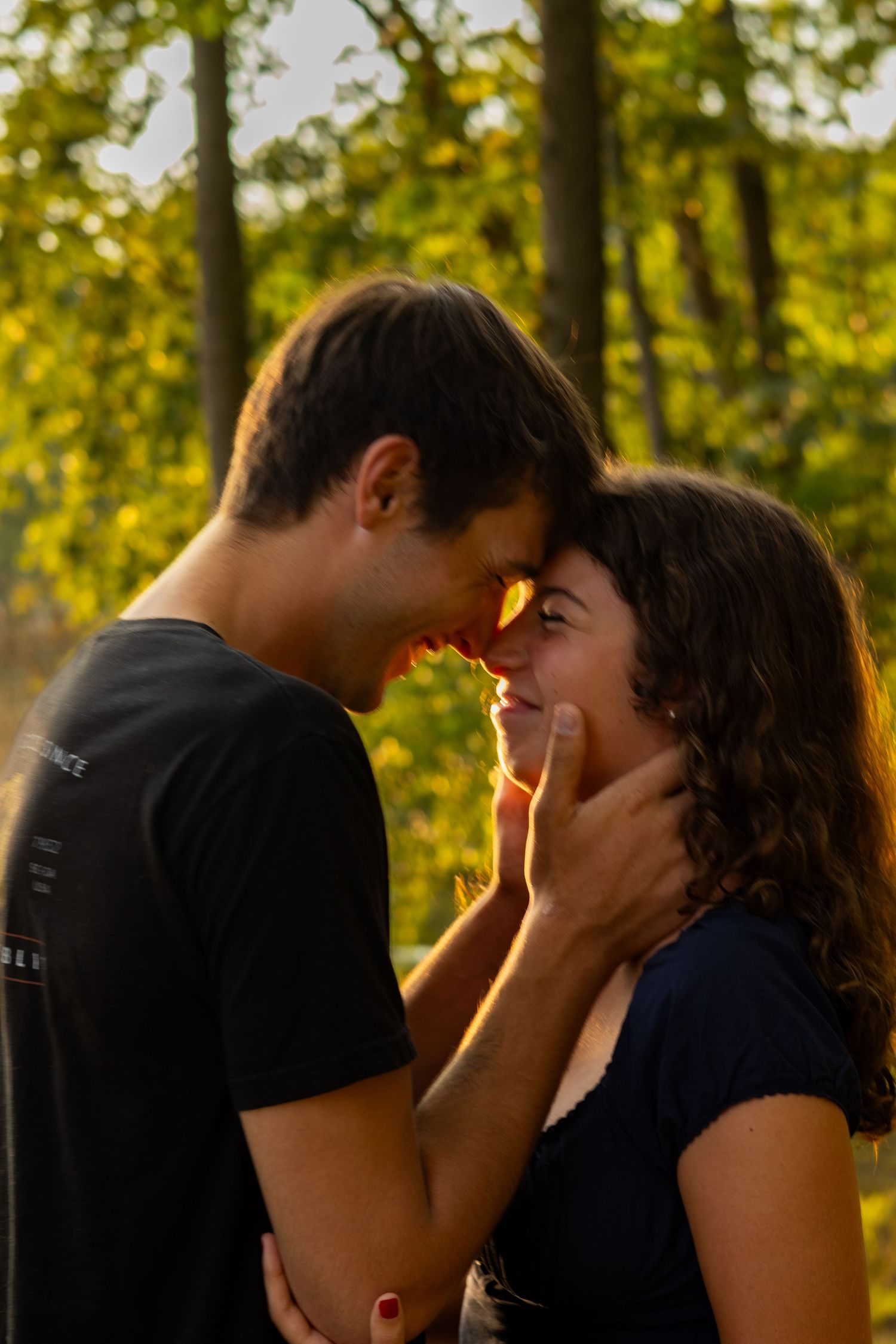 Couple shares intimate moment in golden sunlight against green foliage background in Newark, Delaware.