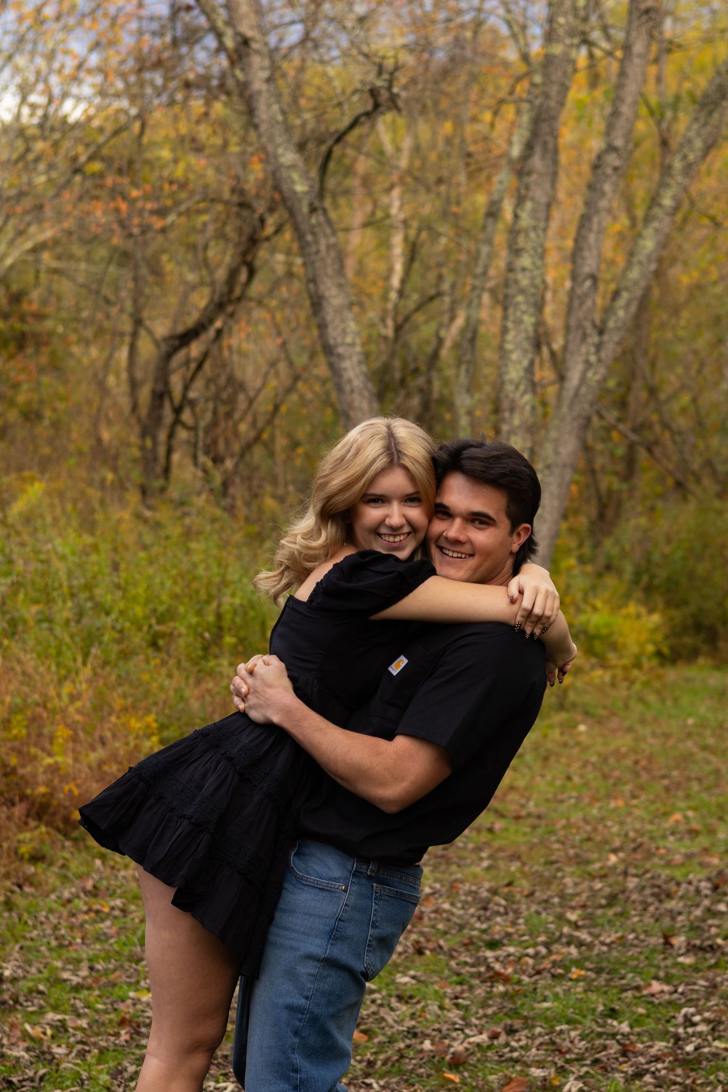 Playful autumn engagement photo in a wooded setting with fall foliage in Newark, Delaware.