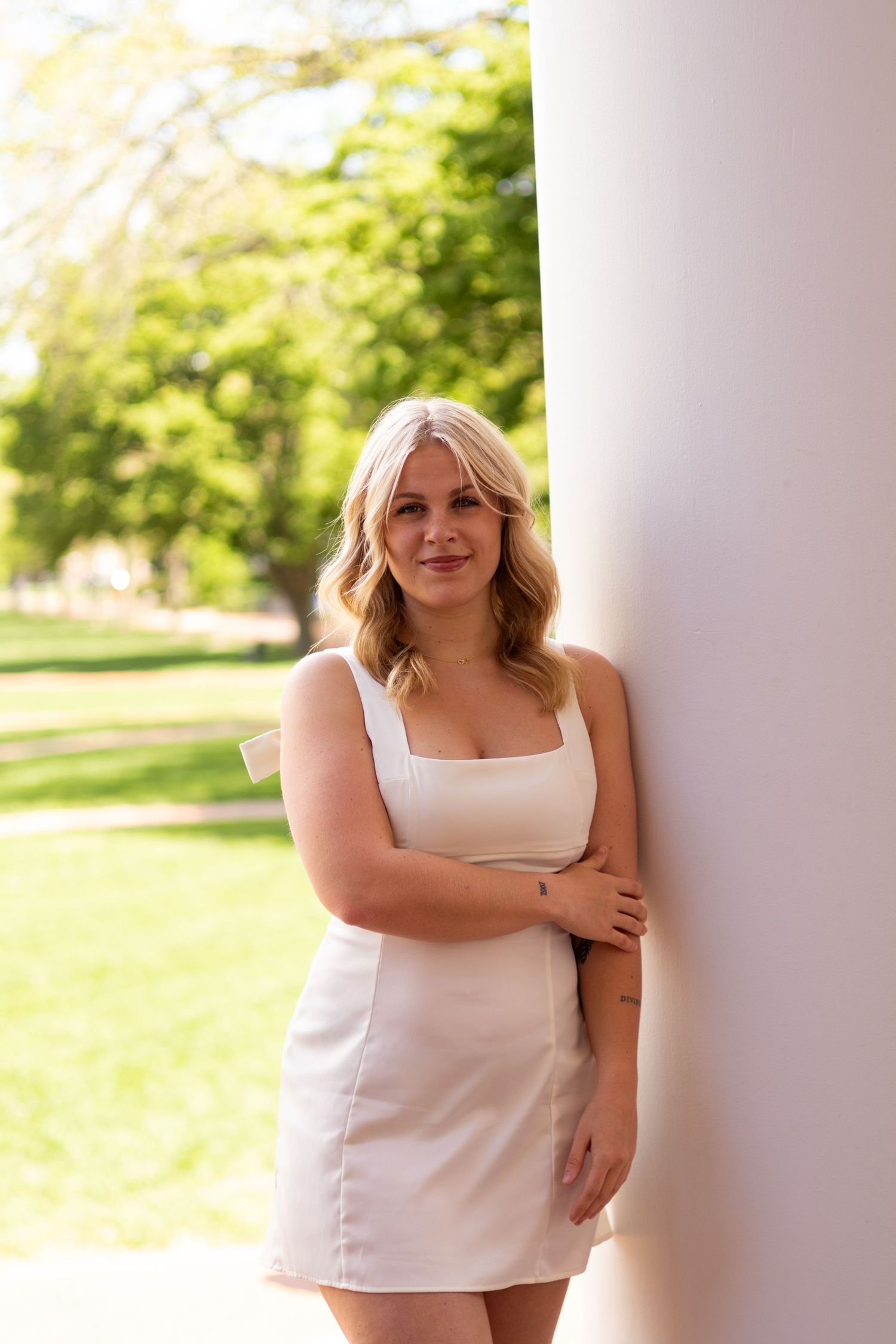 Graduation portraits in white dress against white columns outdoors at the University of Delaware.