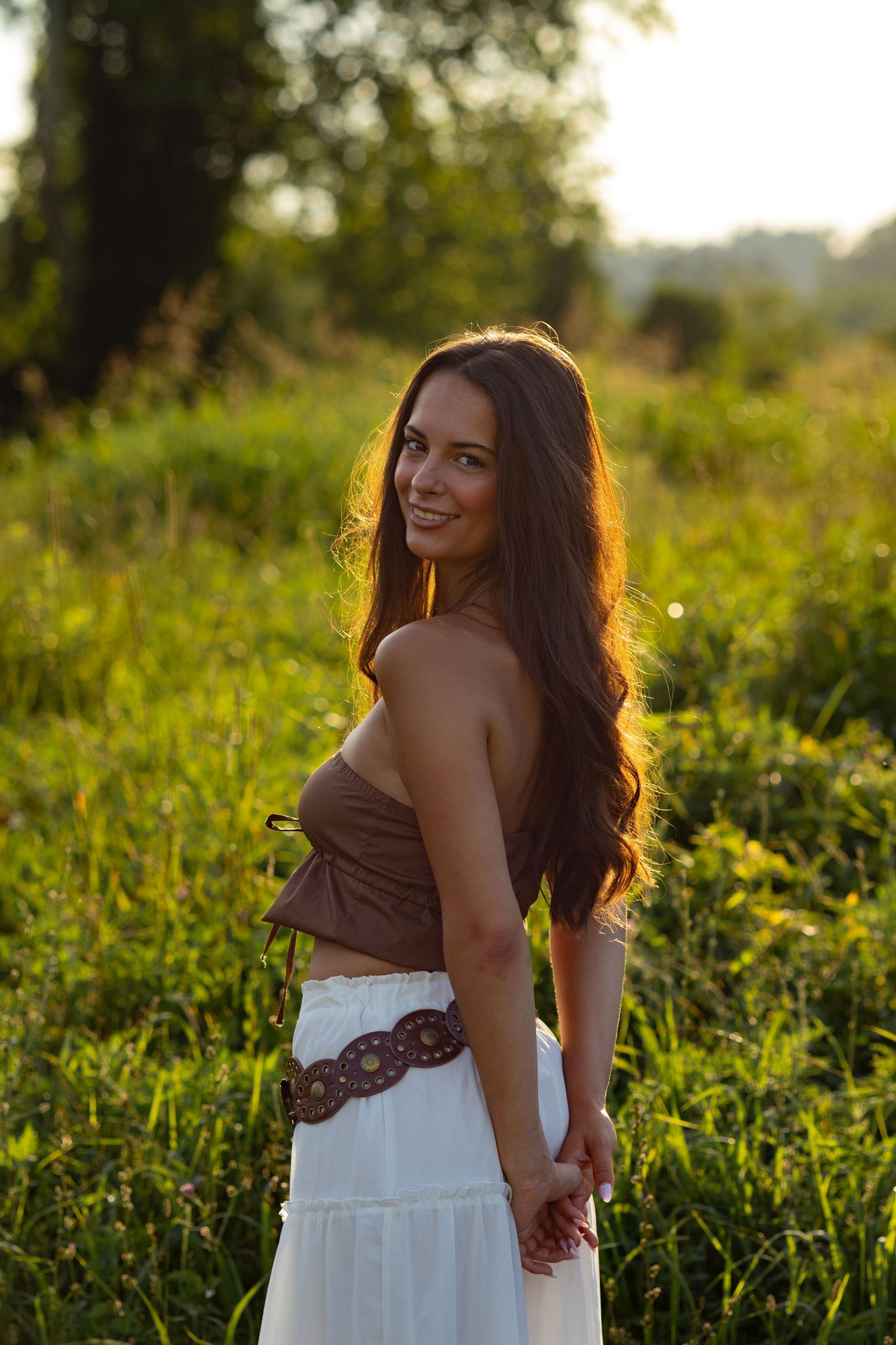 A person in a white and brown dress poses playfully in a field at sunset in Wilmington, Delaware.