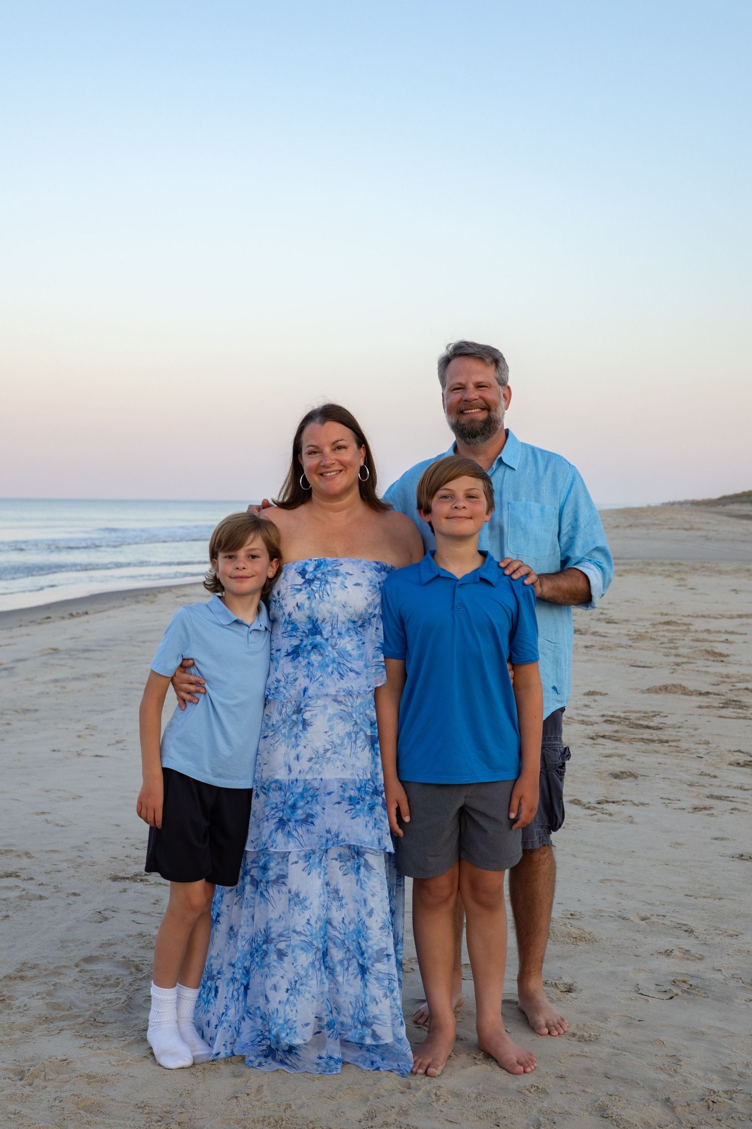 Family wearing coordinated blue outfits poses together on a beach at sunset in Outer Banks, North Carolina.