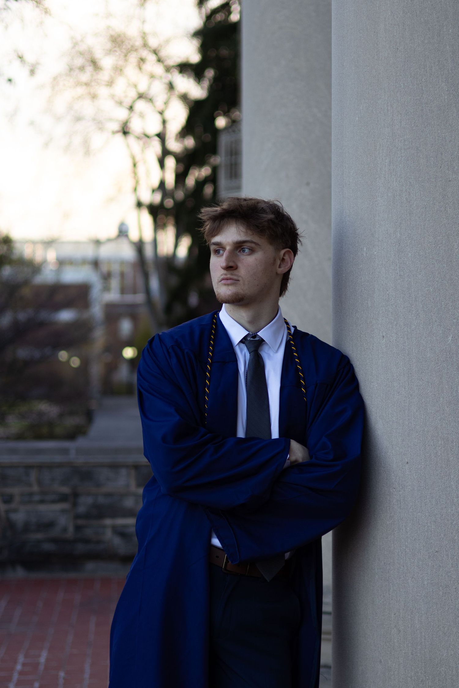Graduate in formal attire leans thoughtfully against classical white column at Penn State University.