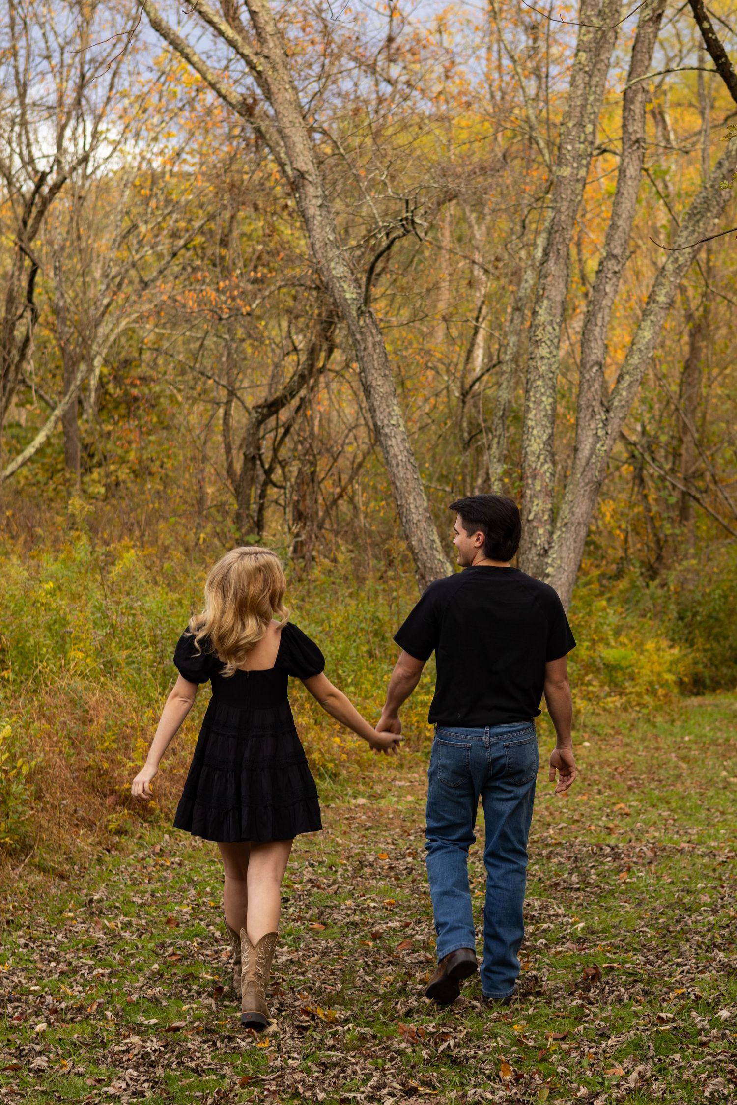 Couple walking together through autumn woods with fallen leaves on ground in Newark, Delaware.