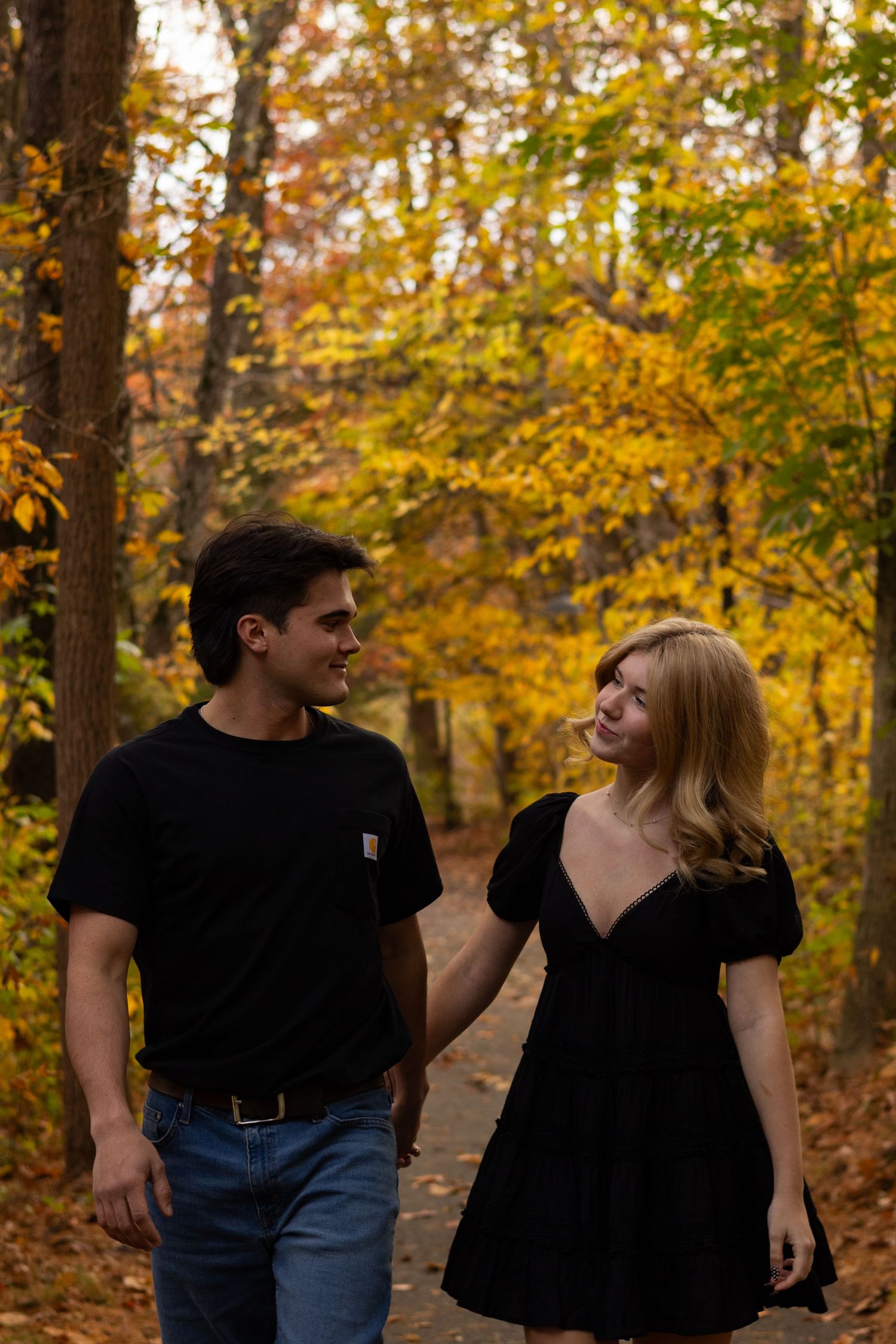 A couple walks through autumn trees wearing black outfits in Newark, Delaware.