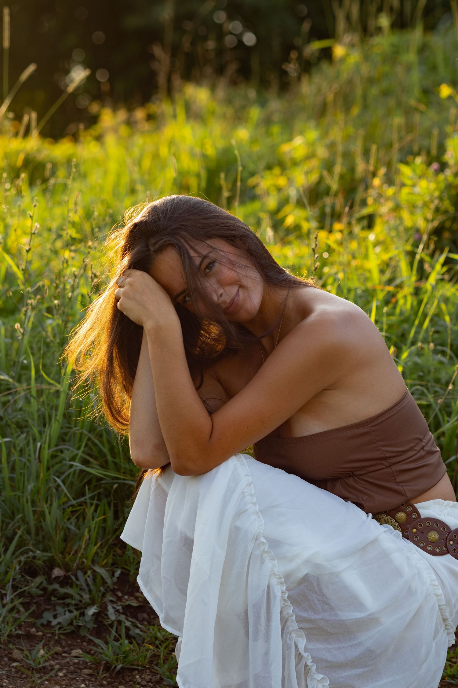 Woman in white dress and brown top posing artistically in a field of wildflowers in Wilmington, Delaware.