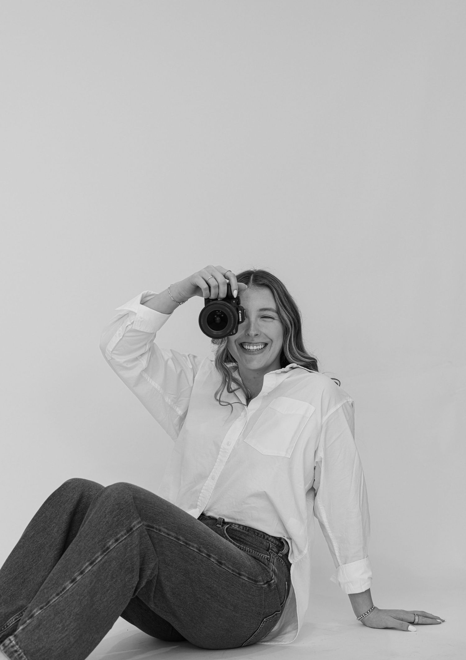 Photographer in white button down shirt and jeans taking a photo while sitting against plain background for Madison Adele Photography.