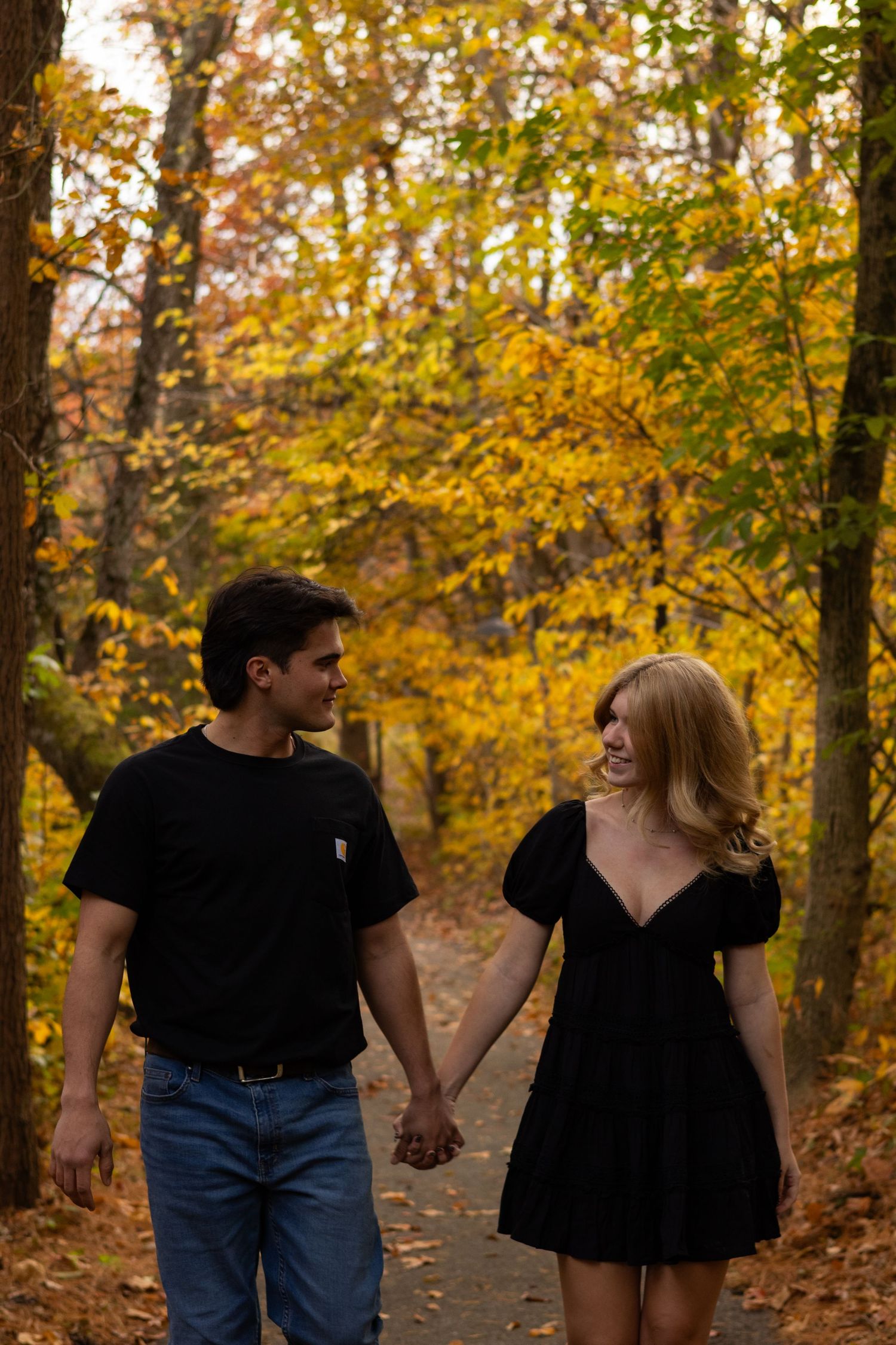 Couple walking hand in hand on a path surrounded by golden fall foliage in Newark, Delaware.