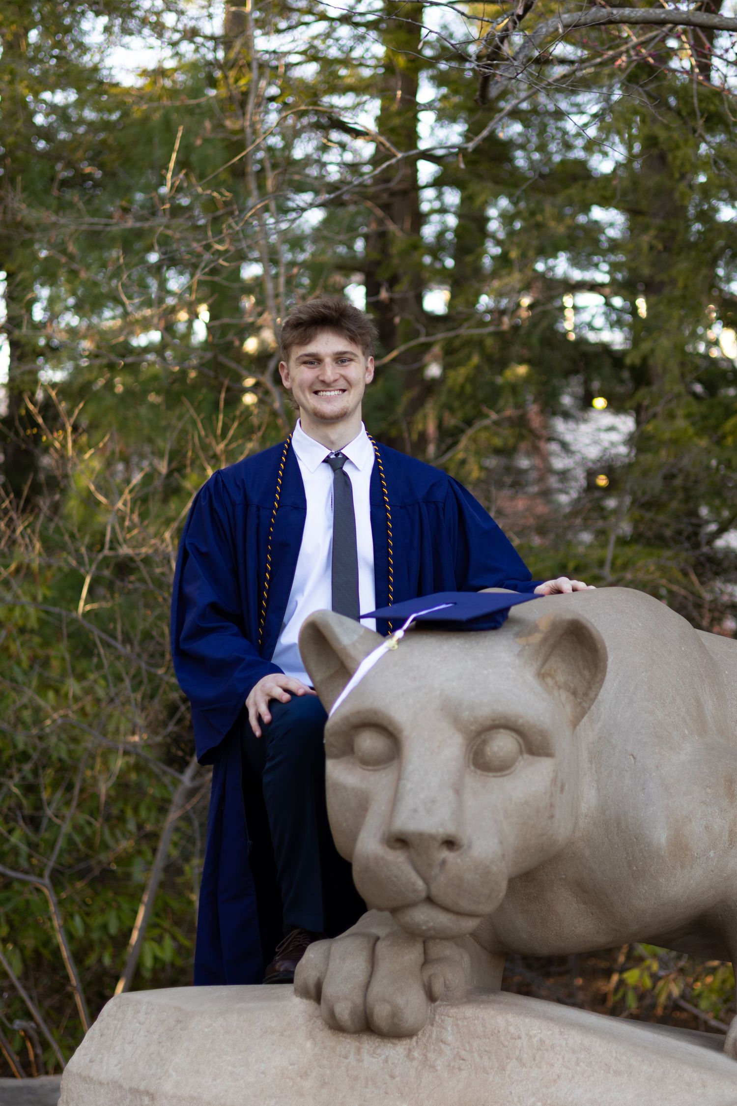 Graduate in academic regalia poses with Penn State Nittany Lion statue at Pennsylvania State University.