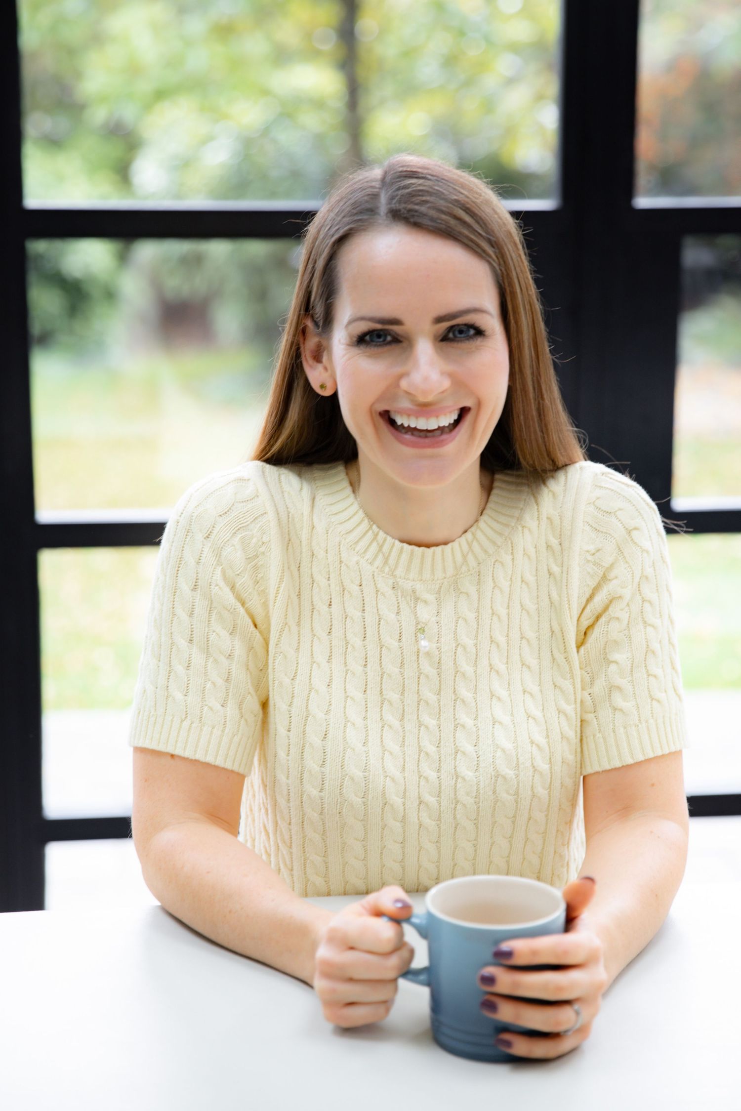 Person wearing cream colored cable knit sweater smiling while looking at phone in bright indoor setting.